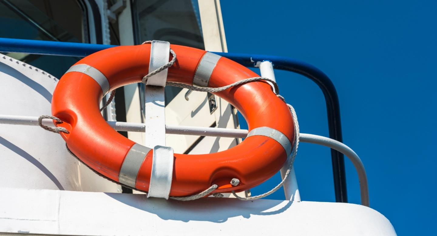 Close-up of a bright orange life ring on a boat against a clear blue sky, symbolizing safety and the importance of proper boat insurance coverage.