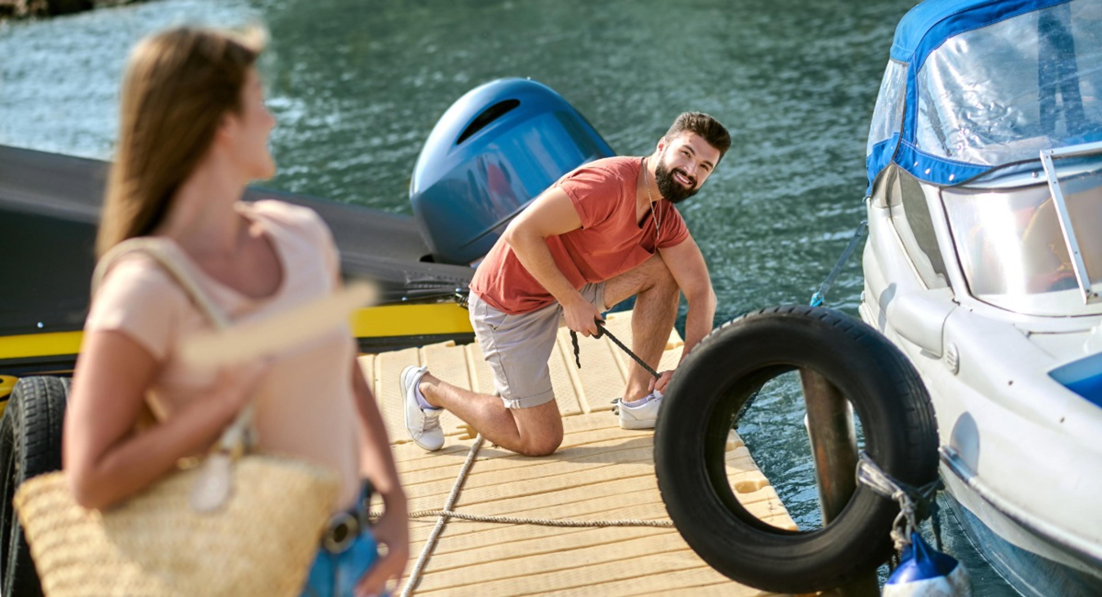 Man securing a boat with dock lines at a marina while a woman watches, demonstrating proactive hurricane season preparation for vessel safety.