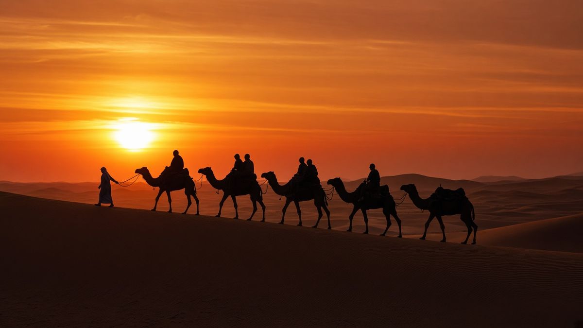 Camel caravan with riders silhouetted on a dune ridge at sunset in the Dubai desert