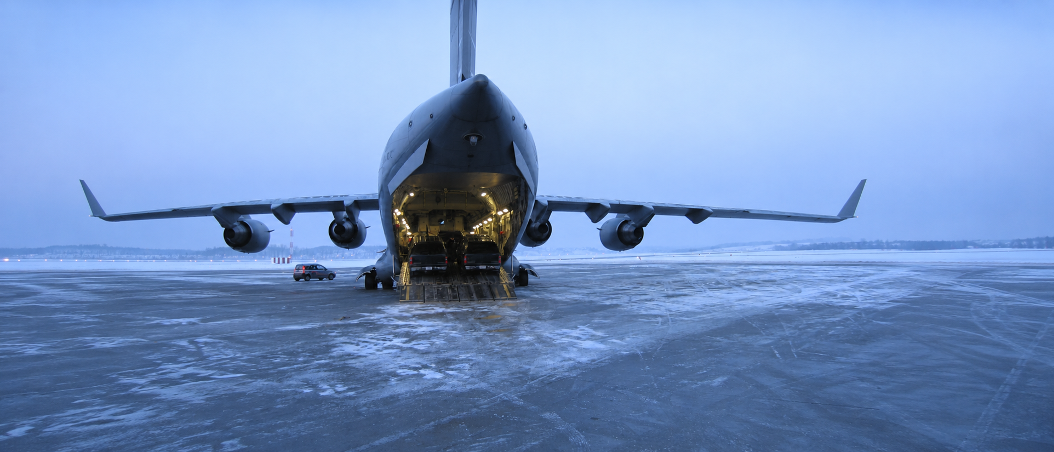 USAF C-17 on the tarmac at dusk; ramp down; black SUVs inside