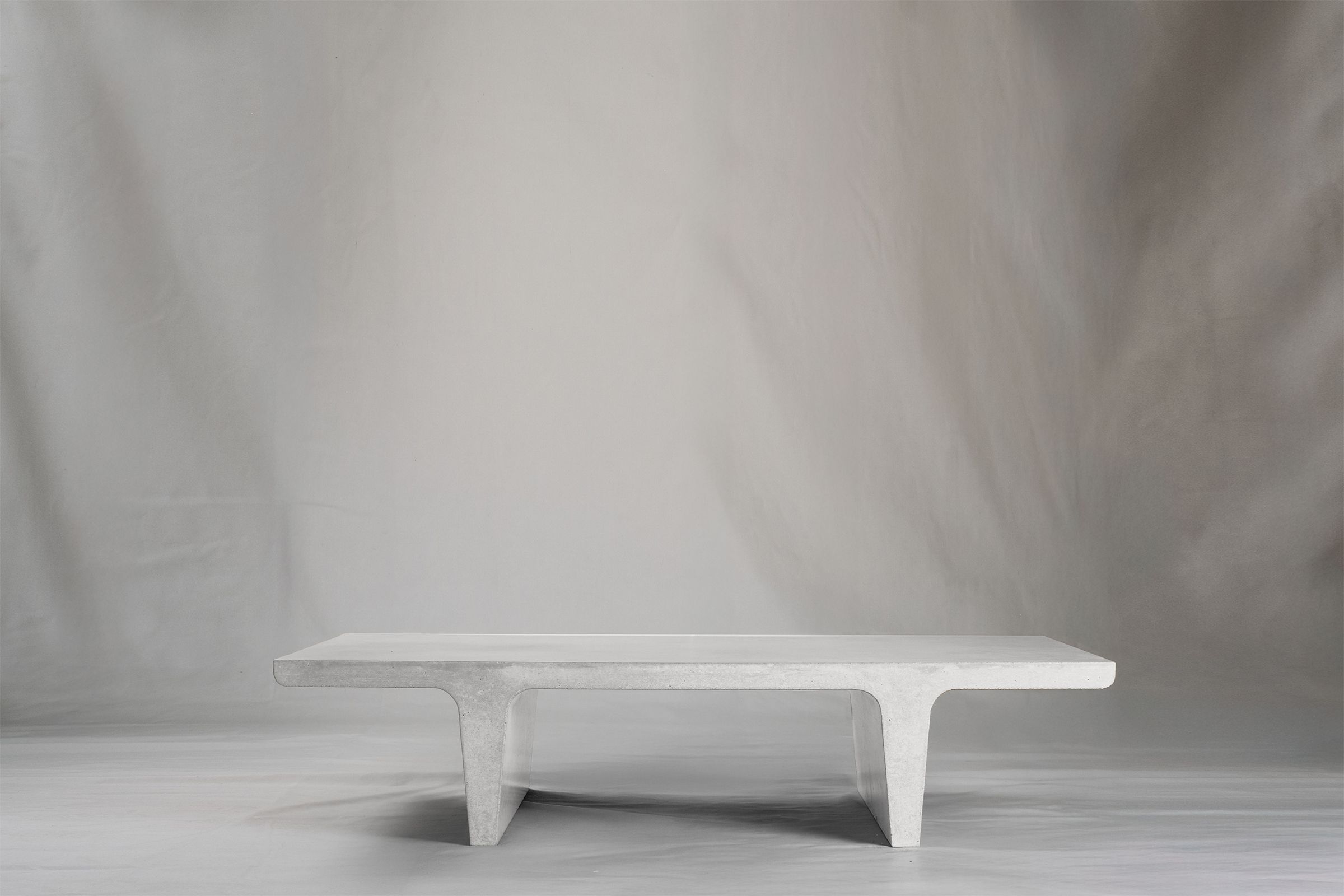Rectangular white chalk concrete coffee table with sculptural double tee legs, featuring a smooth troweled finish, set against a soft neutral backdrop.