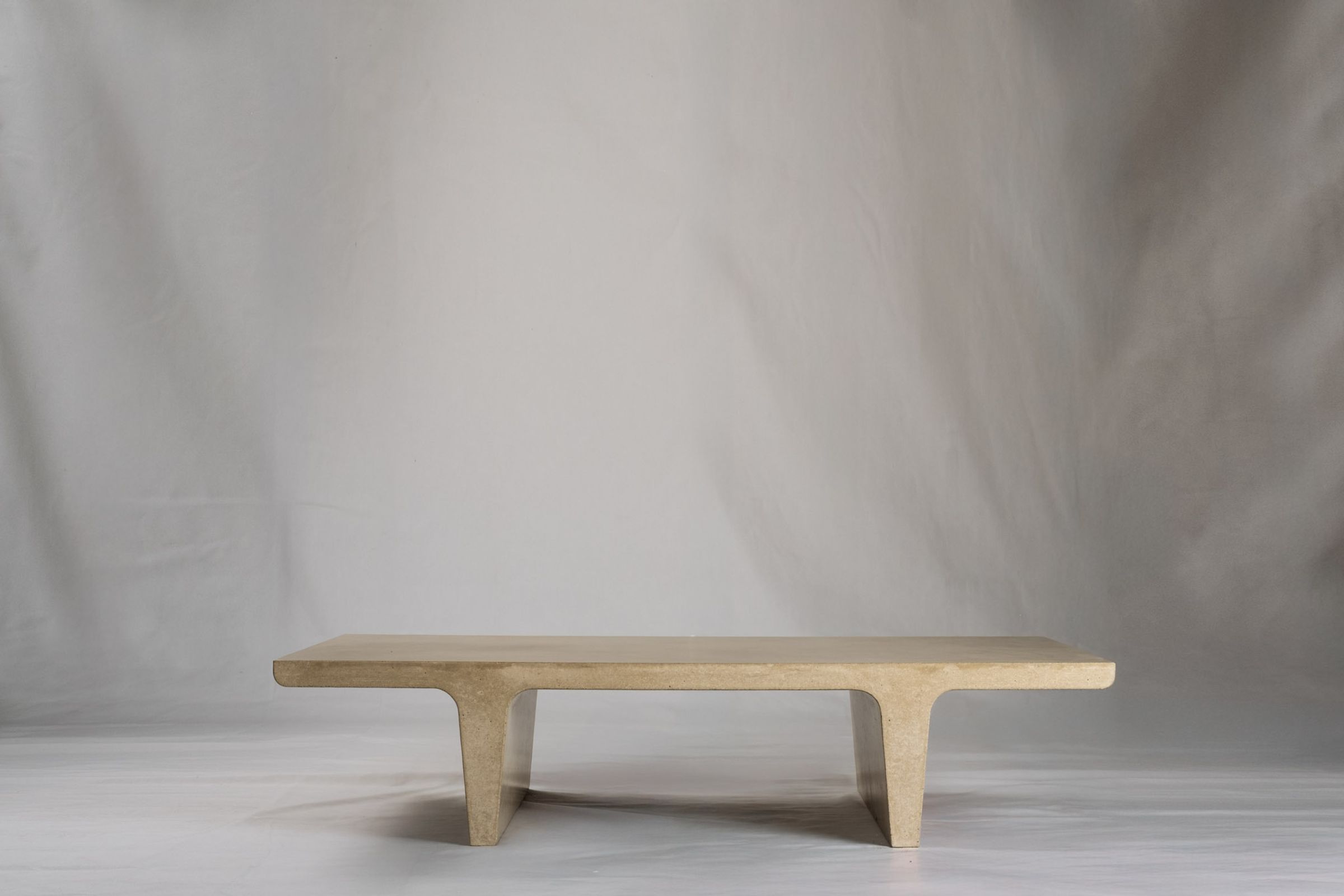 Rectangular light beige concrete coffee table with sculptural double tee legs, featuring a smooth troweled finish, set against a soft neutral backdrop.