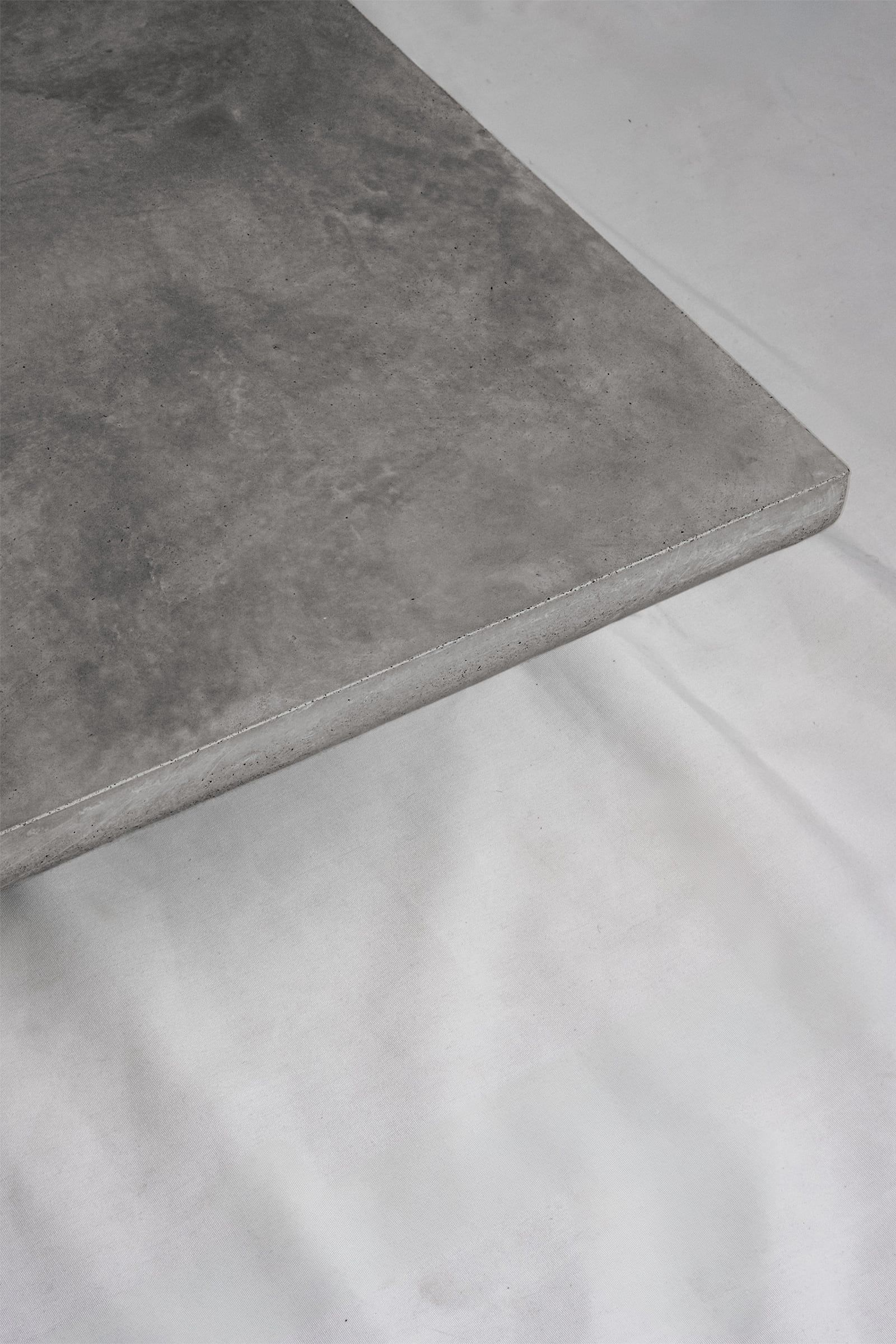 A close up of a dark grey concrete coffee table edge, featuring a smooth troweled finish, set against a soft neutral backdrop.