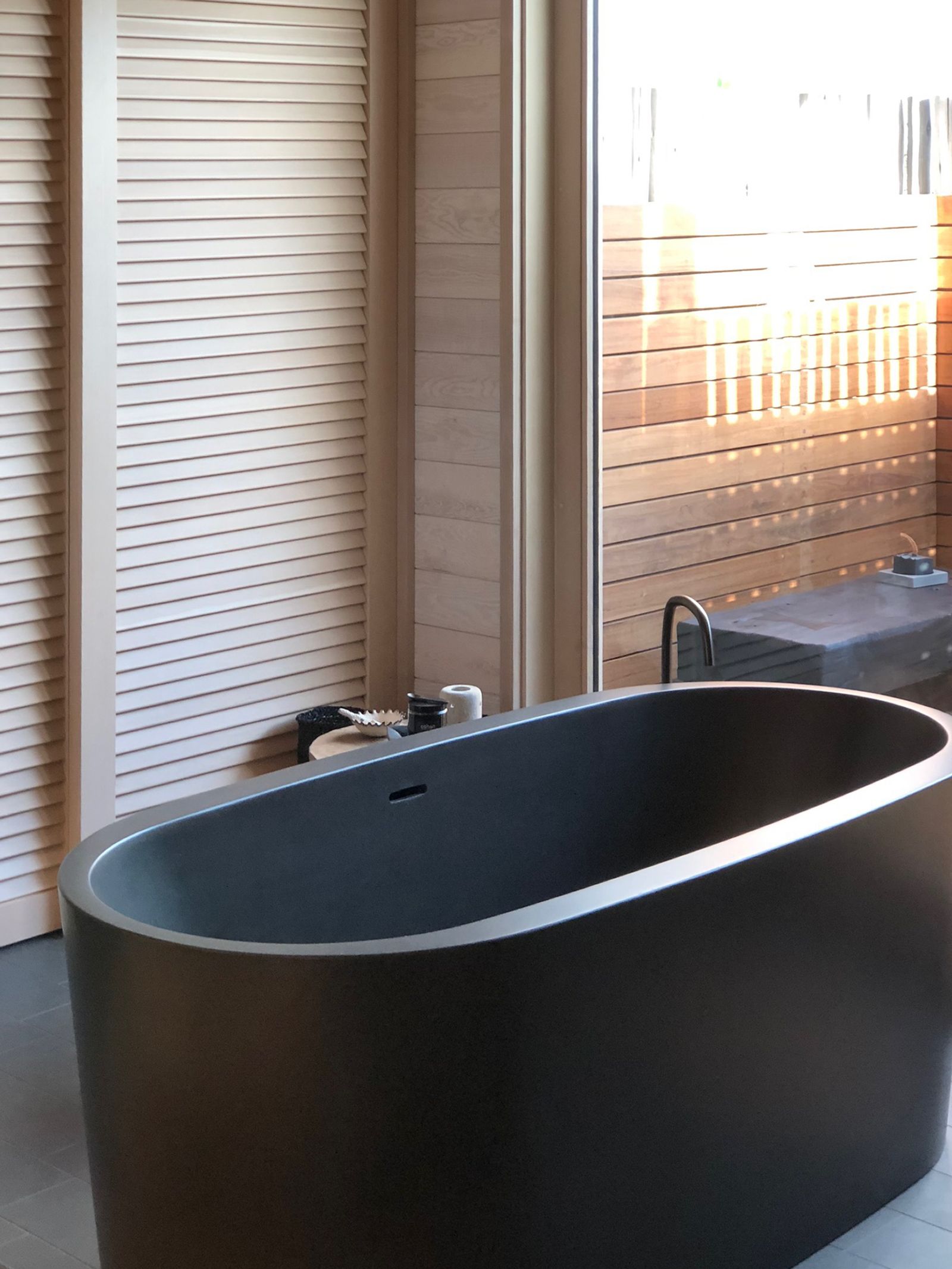 Dark grey concrete bathtub next to a window and wooden panels.