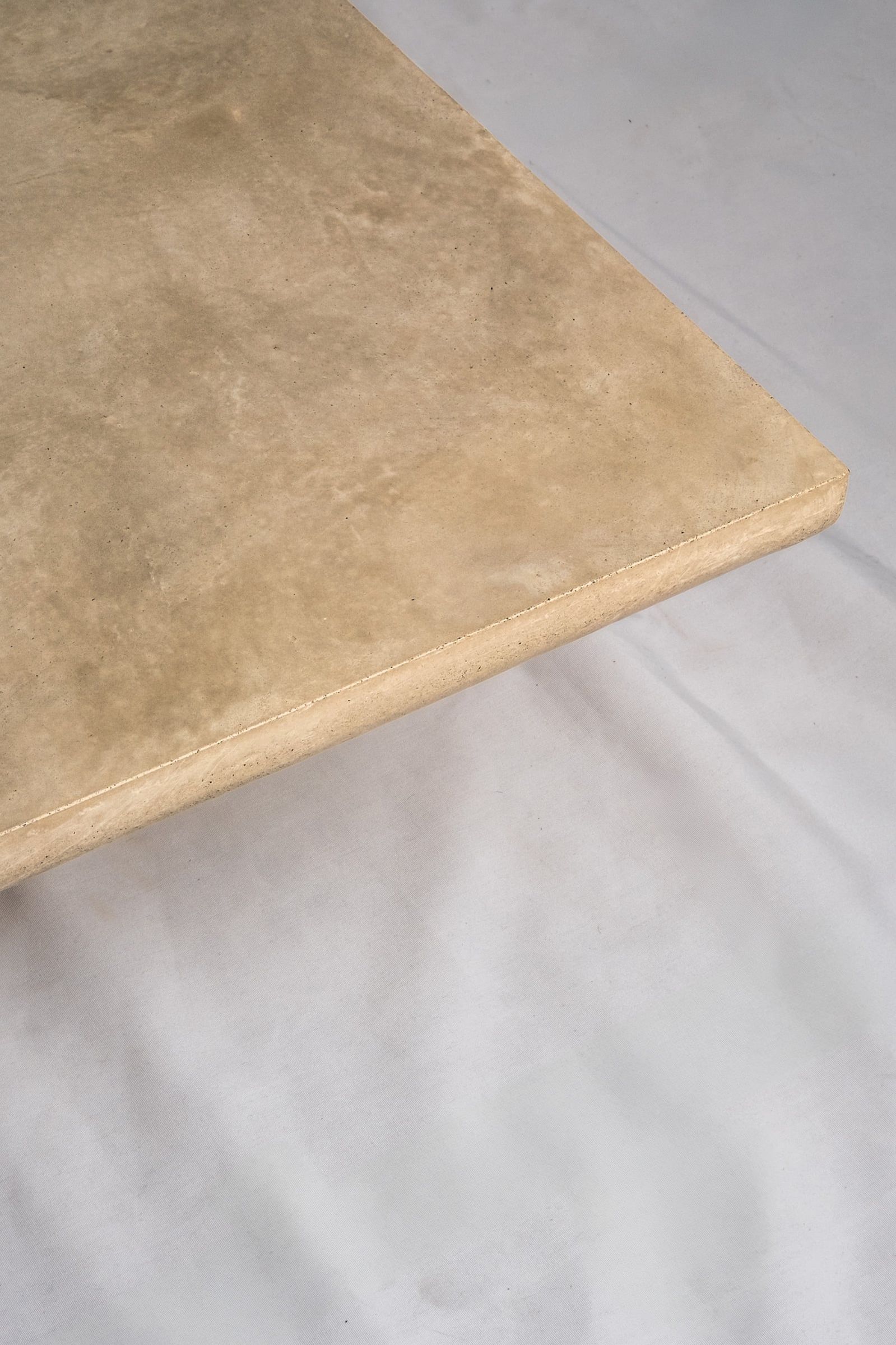 A close up of a light beige concrete coffee table edge, featuring a smooth troweled finish, set against a soft neutral backdrop.