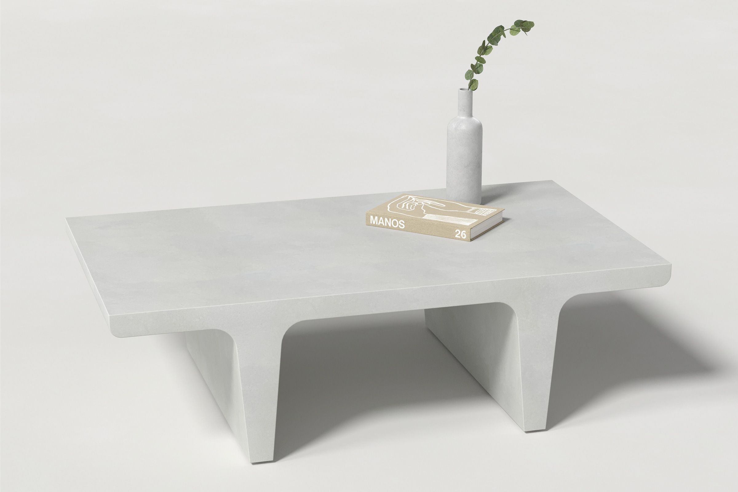 Rectangular white concrete coffee table with sculptural double tee legs, styled with a neutral-toned book and a slender vase holding delicate eucalyptus, set against a clean white background.