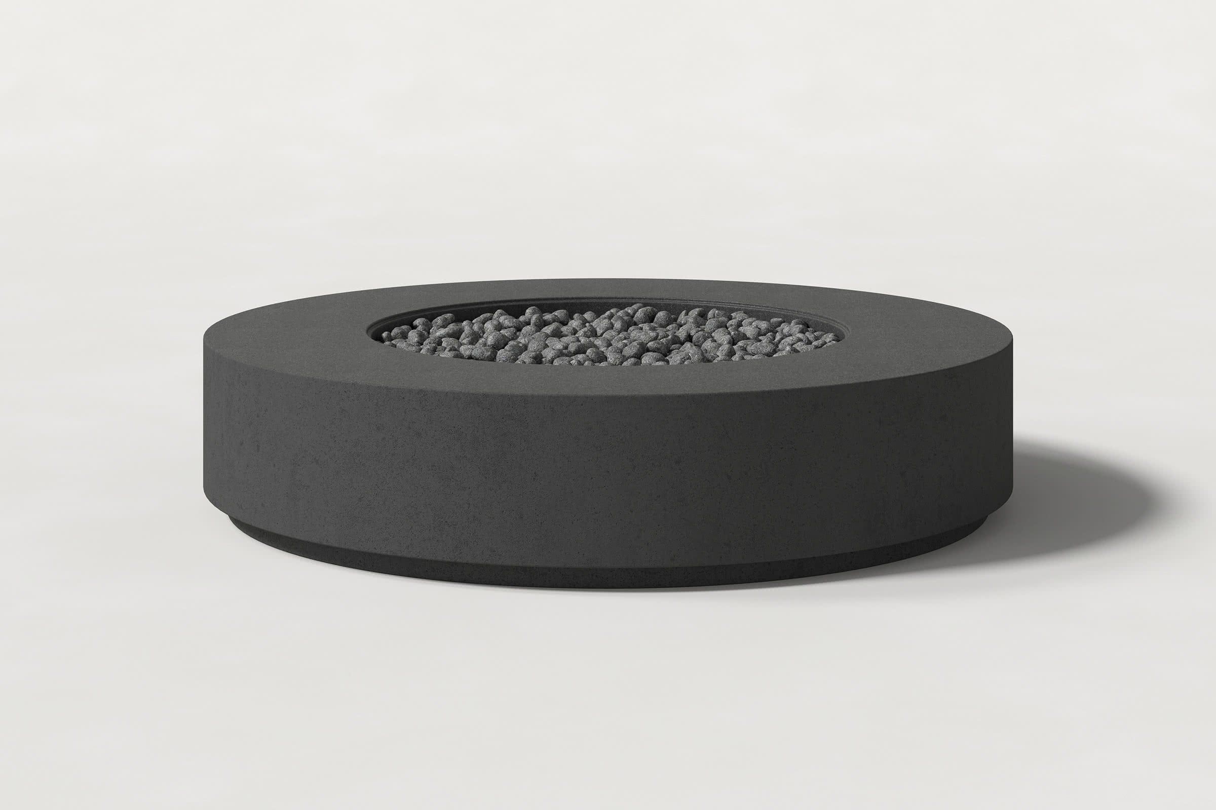 Low cylindrical charcoal concrete fire pit with thick walls and a central circular well filled with dark volcanic rocks. Side view on a white background with a shadow to the right.