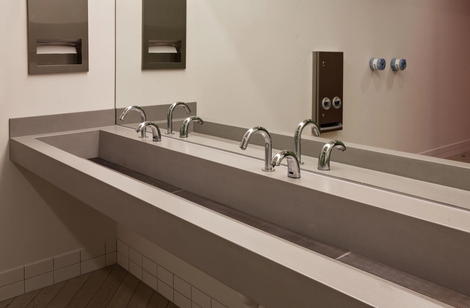 Commercial restroom with extended trough sink and sleek chrome fixtures.