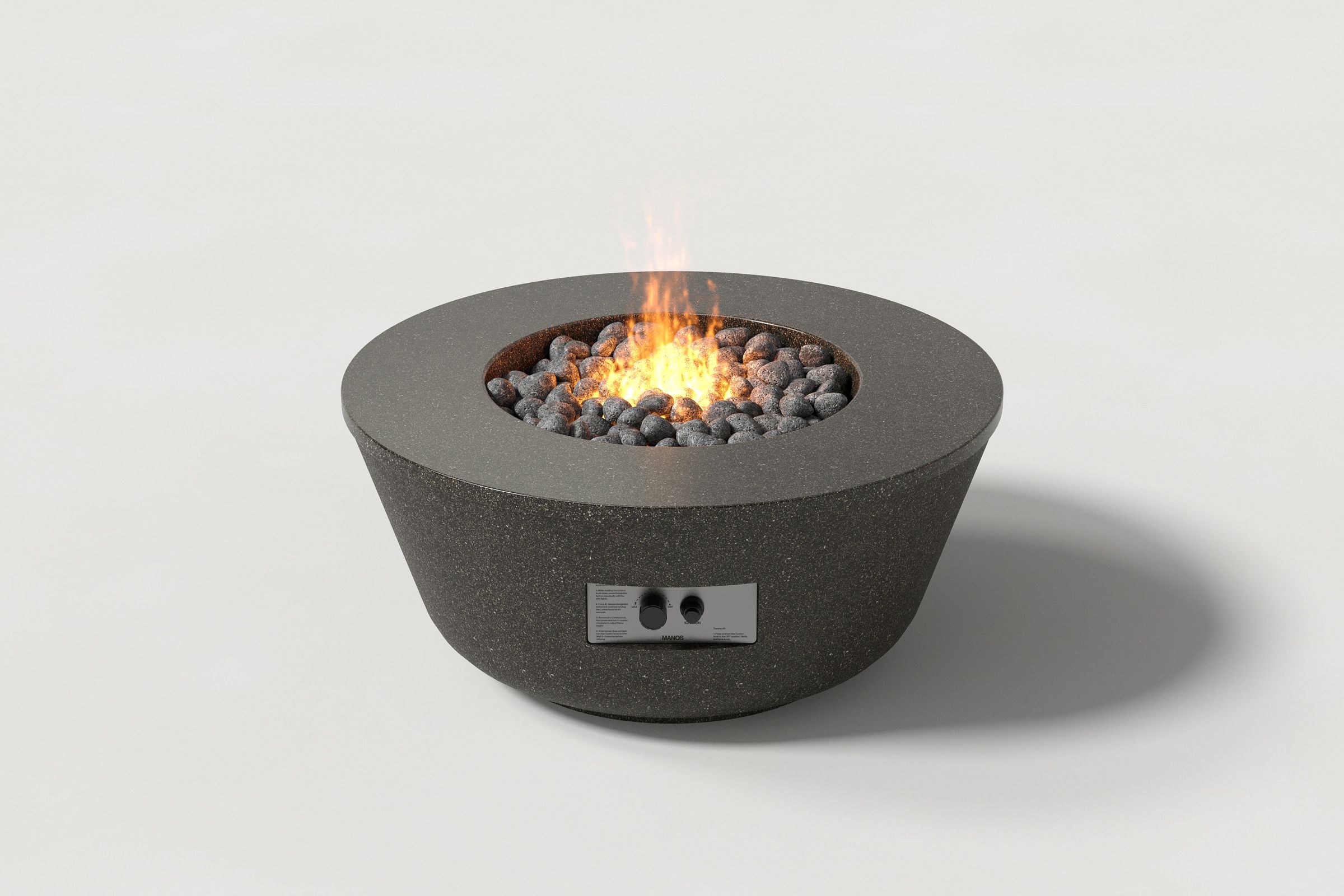 Round dark grey concrete fire pit with a honed top and etched sides, featuring exposed lava rocks and an active flame without the glass shield, set against a clean white background.