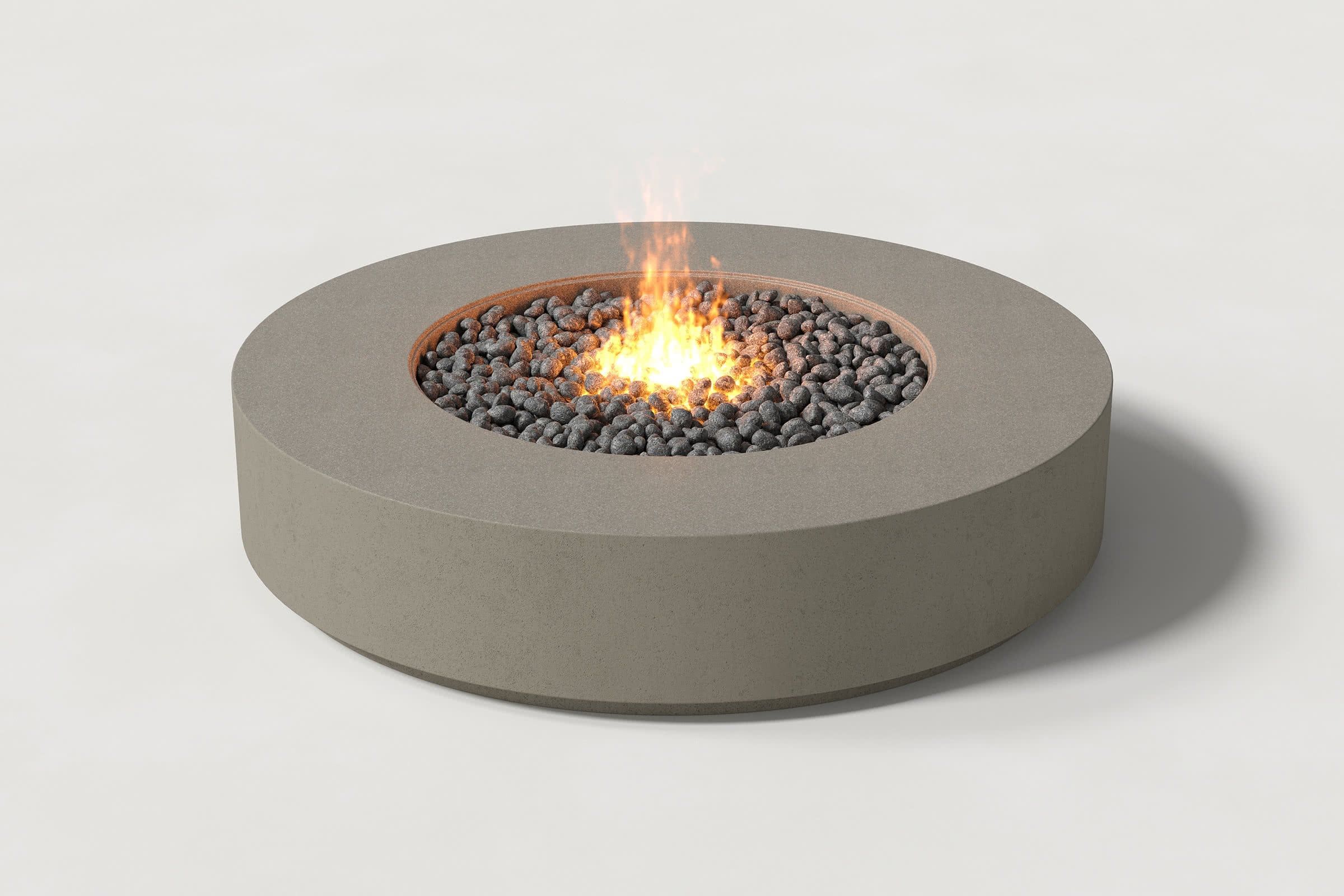 Low cylindrical dark grey concrete fire pit with thick walls and a central circular well. Mid-range angle shows the well filled with flaming volcanic rocks against a white background.