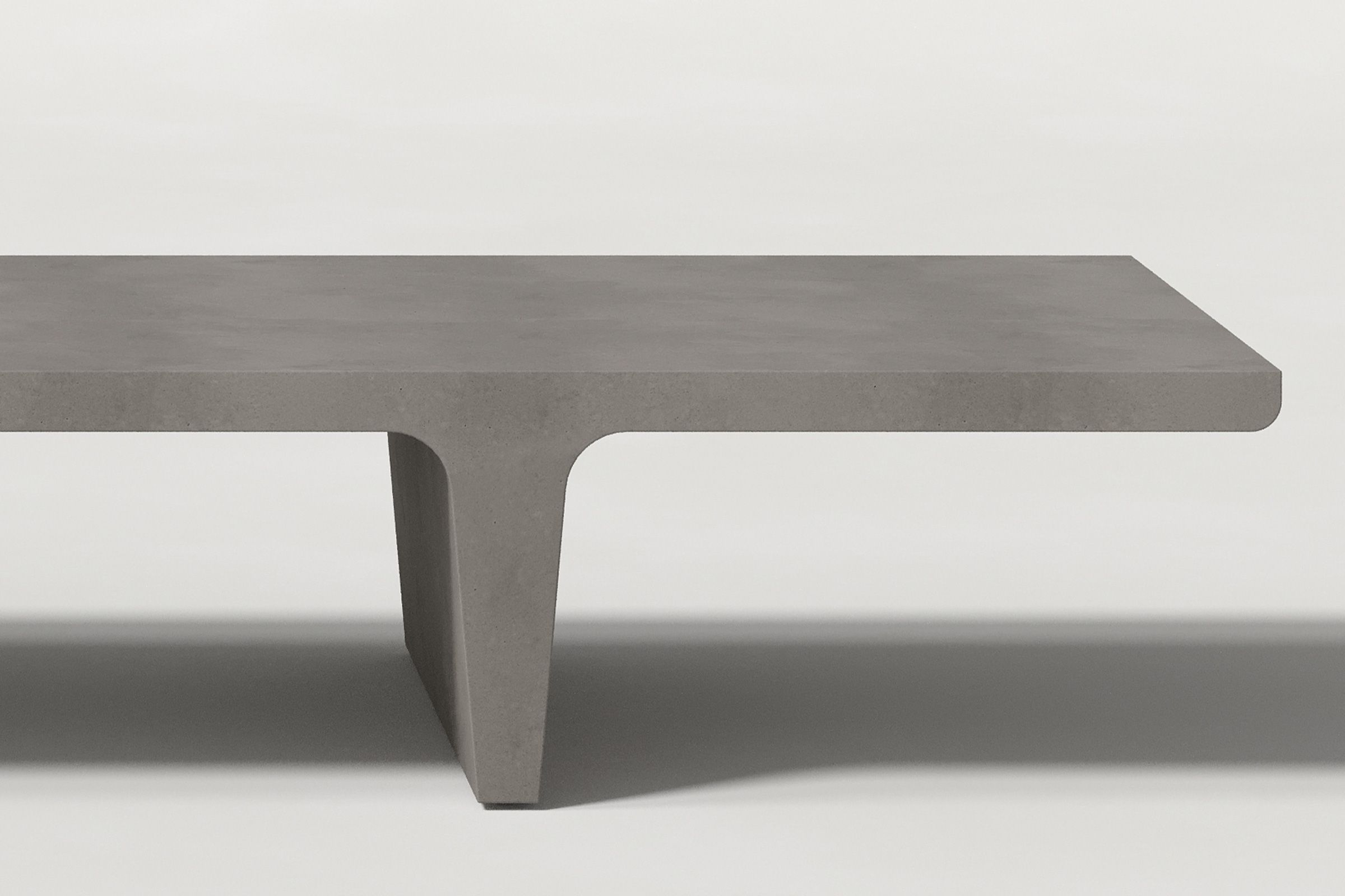 Close-up of a dark grey concrete coffee table with sculptural double tee legs, highlighting soft edges and subtle surface texture against a clean white background.