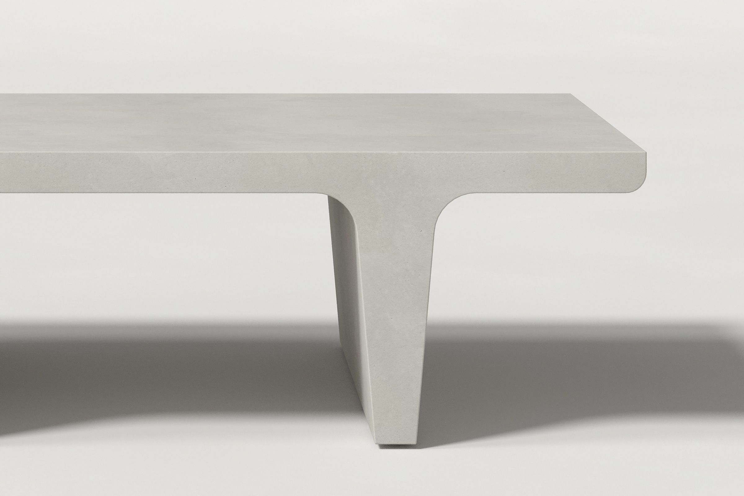 Close-up of a light grey concrete coffee table with sculptural double tee legs, highlighting soft edges and subtle surface texture against a clean white background.