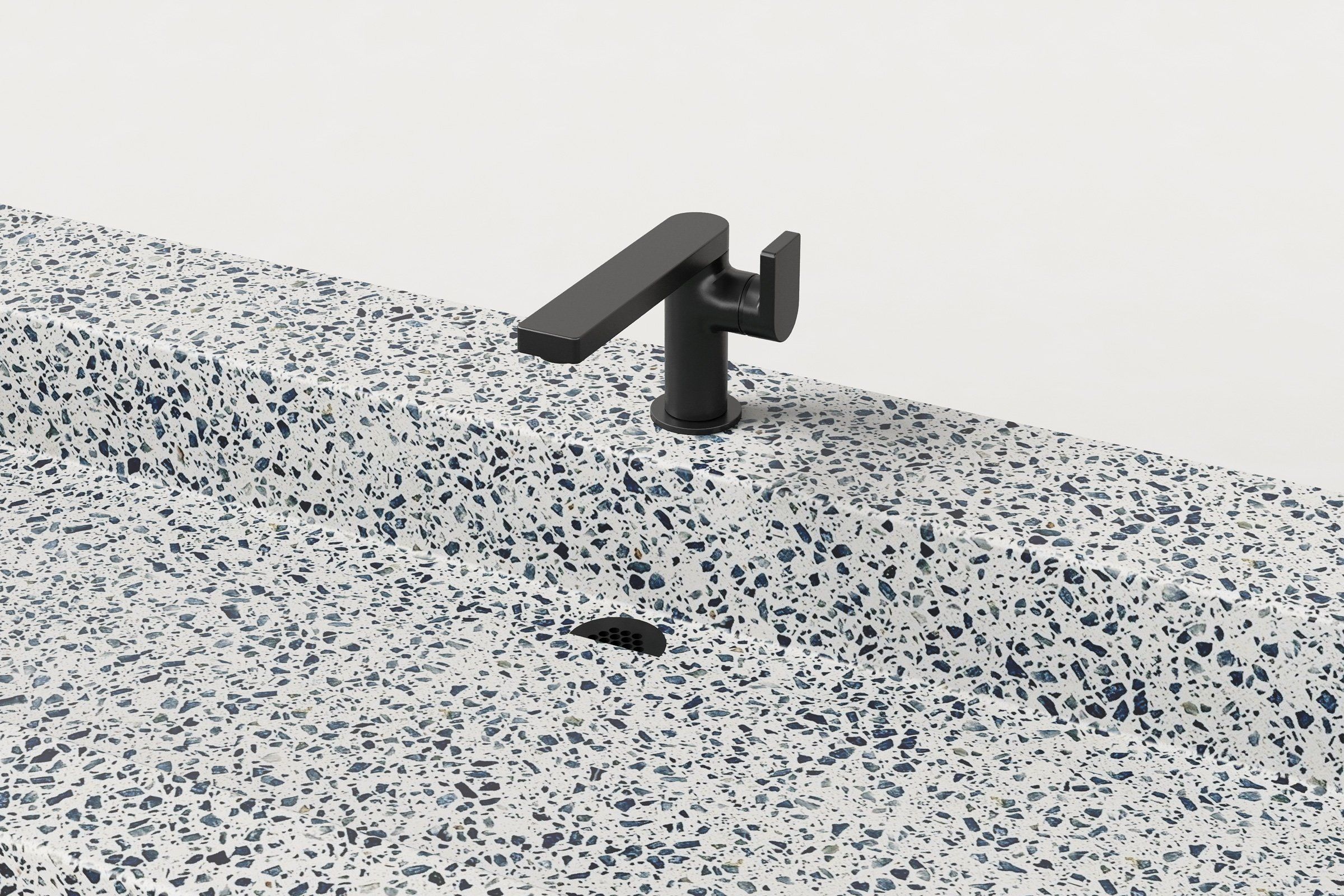 Close-up of matte black faucet on terrazzo sink showing speckled surface and drain detail.