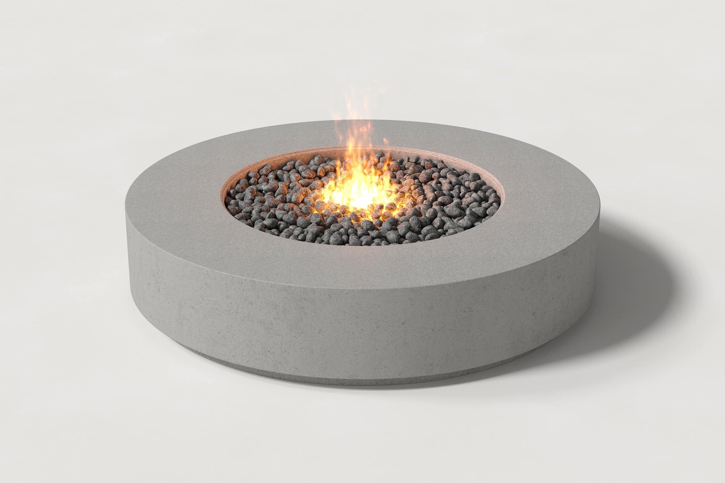 Low cylindrical grey concrete fire pit with thick walls and a central circular well. Mid-range angle shows the well filled with flaming volcanic rocks against a white background.