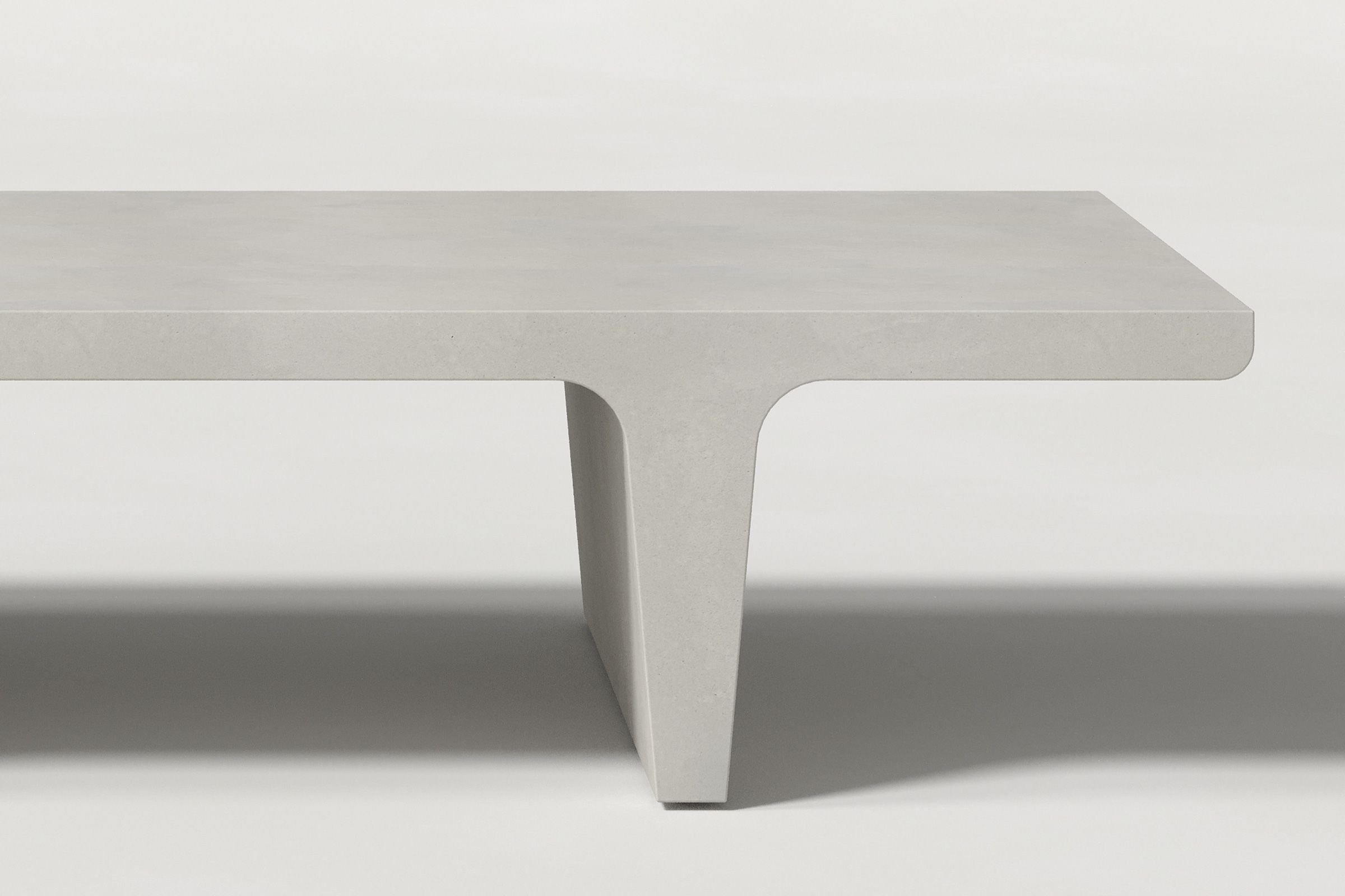 Close-up of a light grey concrete coffee table with sculptural double tee legs, highlighting soft edges and subtle surface texture against a clean white background.