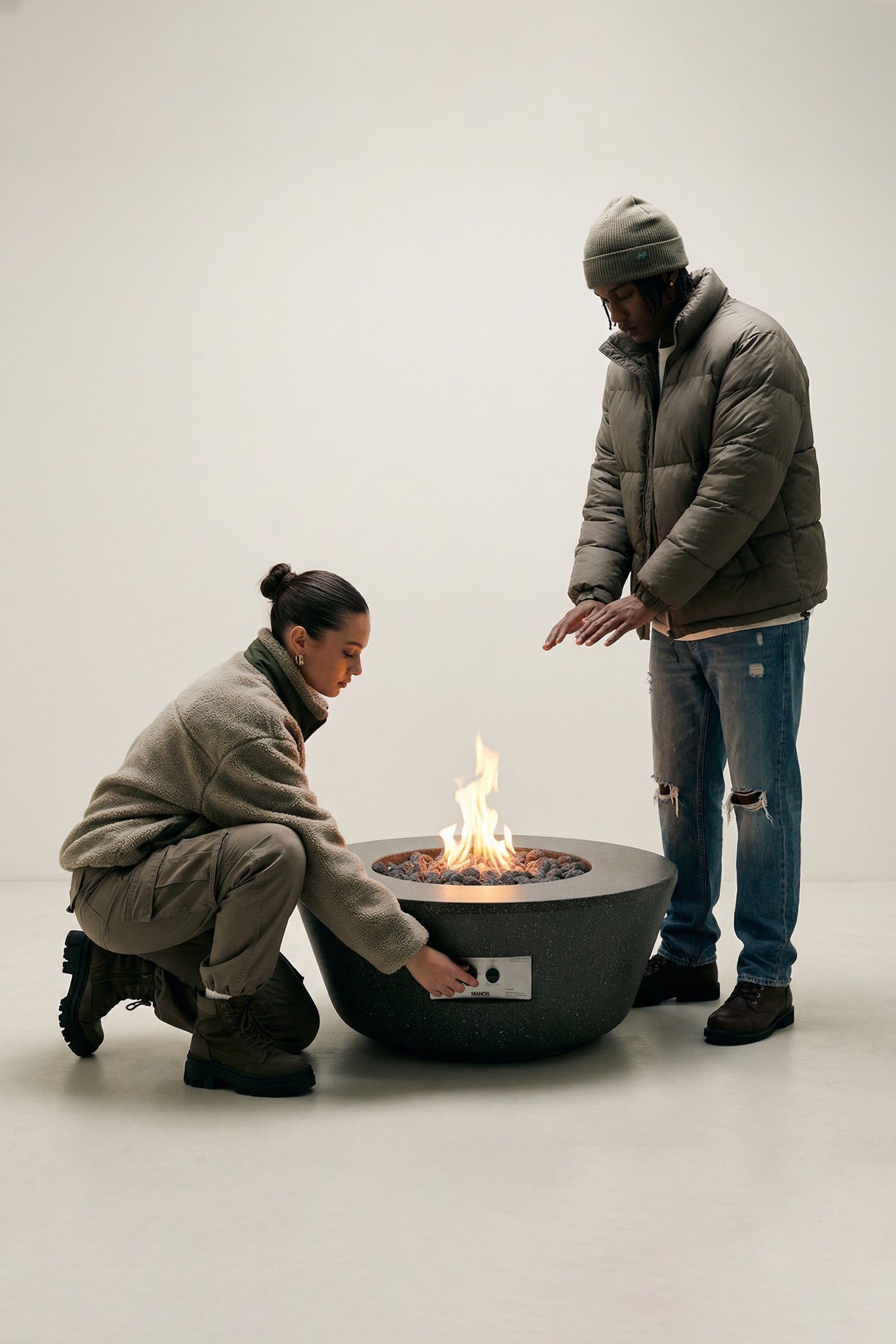 Rosa concrete fire table with active flame, two people adjusting controls and warming hands around it.