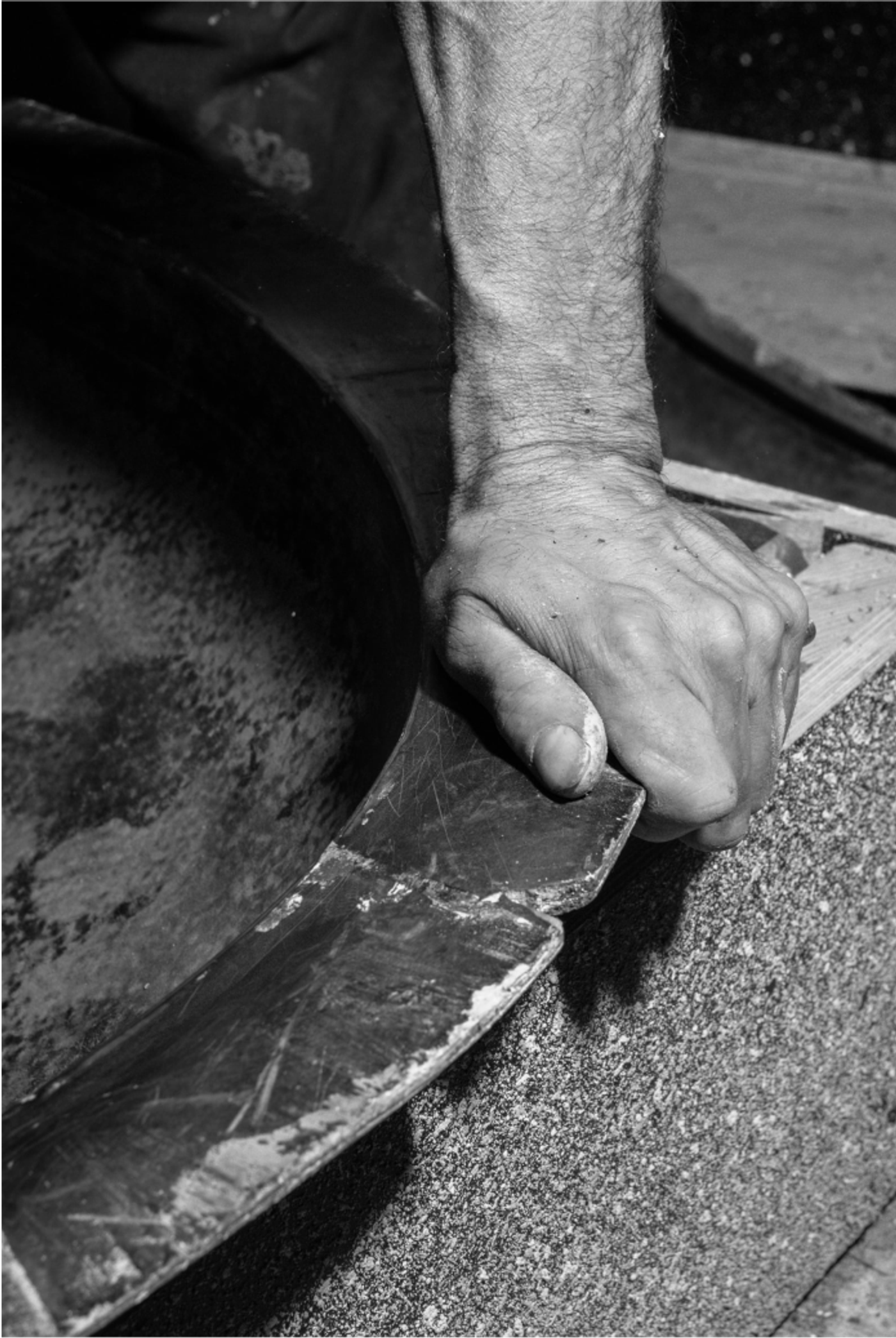 Greyscale close-up of a weathered hand holding a worn tool against a textured surface, showing craftsmanship at work