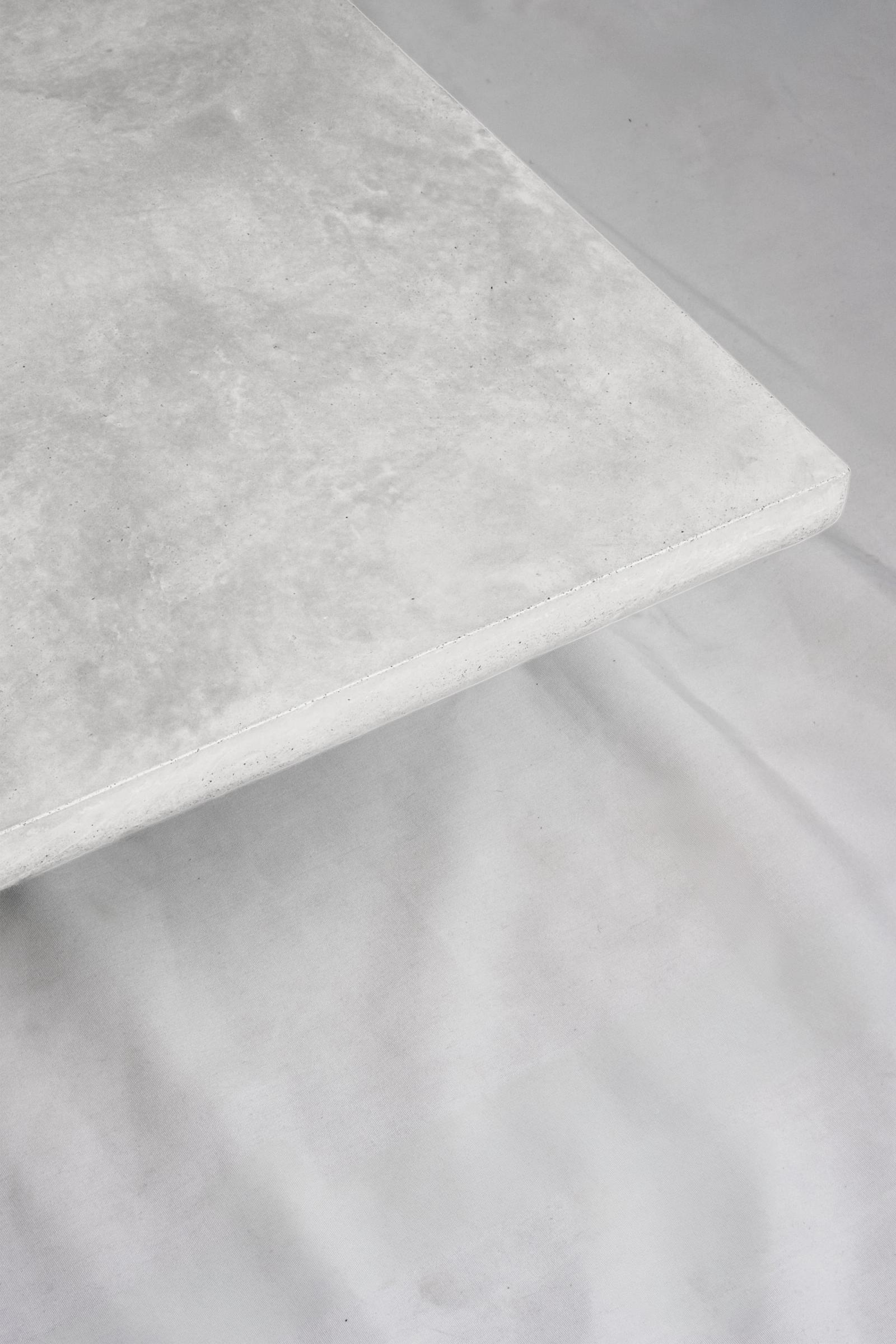 A close up of a chalk white concrete coffee table edge, featuring a smooth troweled finish, set against a soft neutral backdrop.