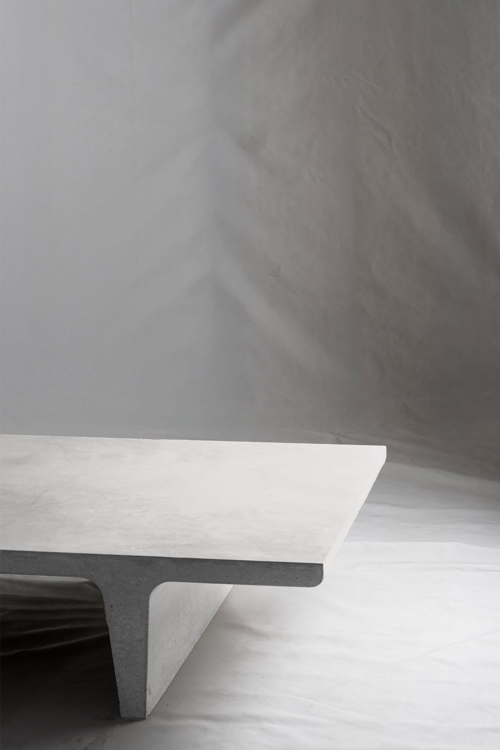 A close up of a chalk white concrete coffee table with sculptural double tee legs, featuring a smooth troweled finish, set against a soft neutral backdrop.