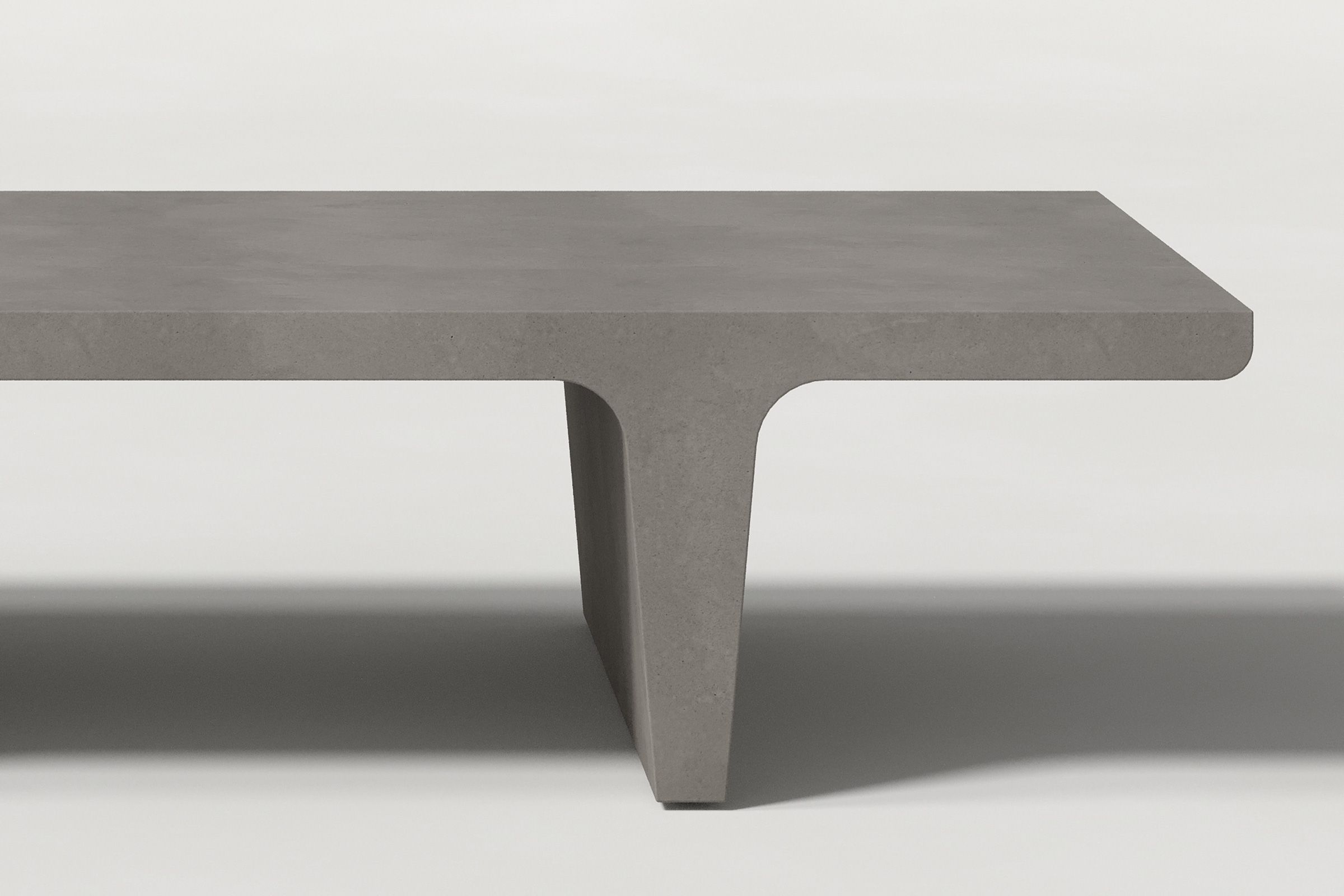 Close-up of a dark grey concrete coffee table with sculptural double tee legs, highlighting soft edges and subtle surface texture against a clean white background.