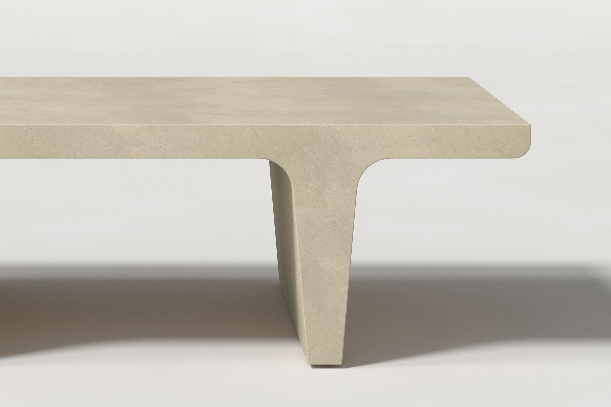Close-up of a light beige concrete coffee table with sculptural double tee legs, highlighting soft edges and subtle surface texture against a clean white background.