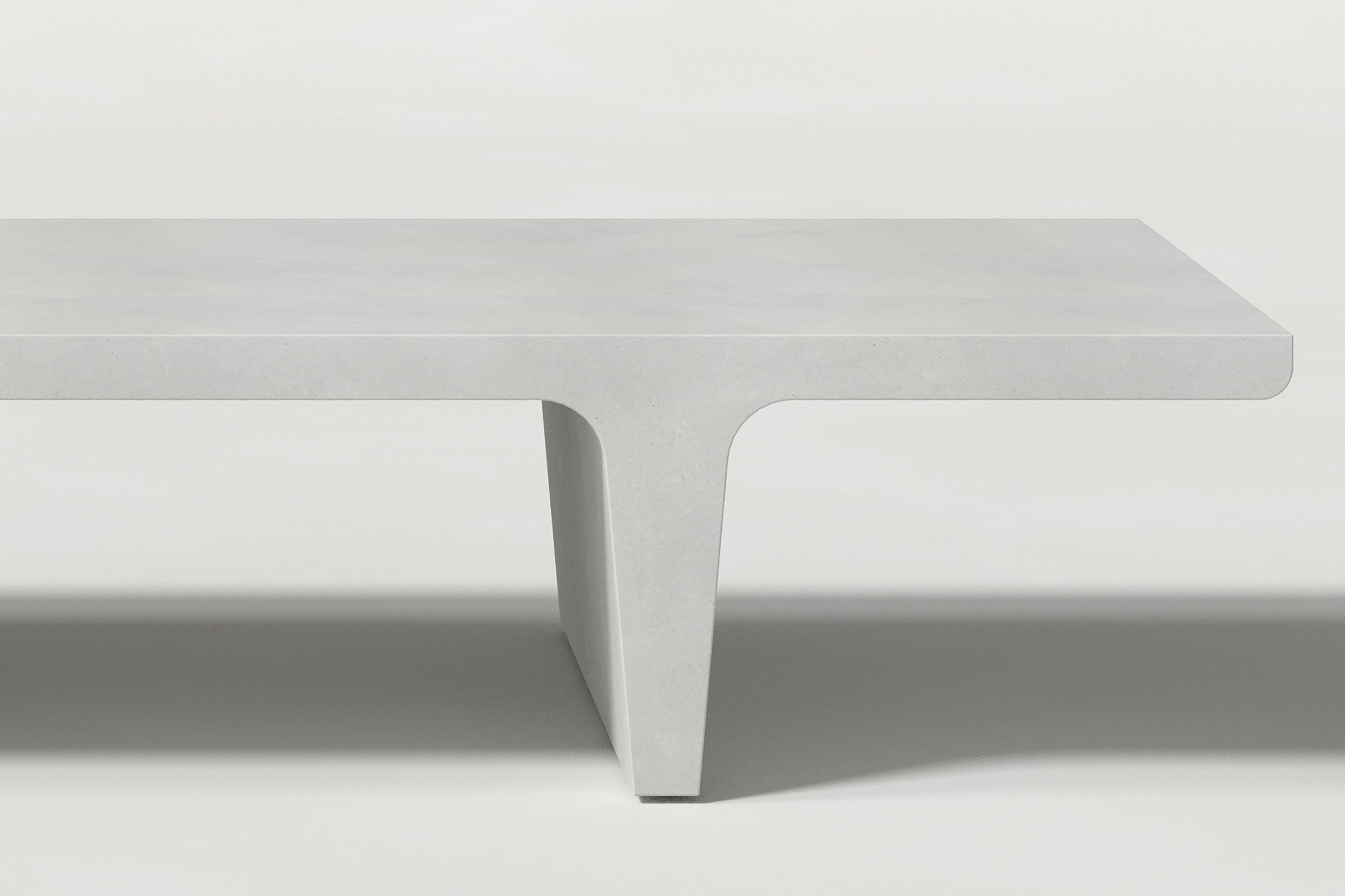 Close-up of a white concrete coffee table with sculptural double tee legs, highlighting soft edges and subtle surface texture against a clean white background.