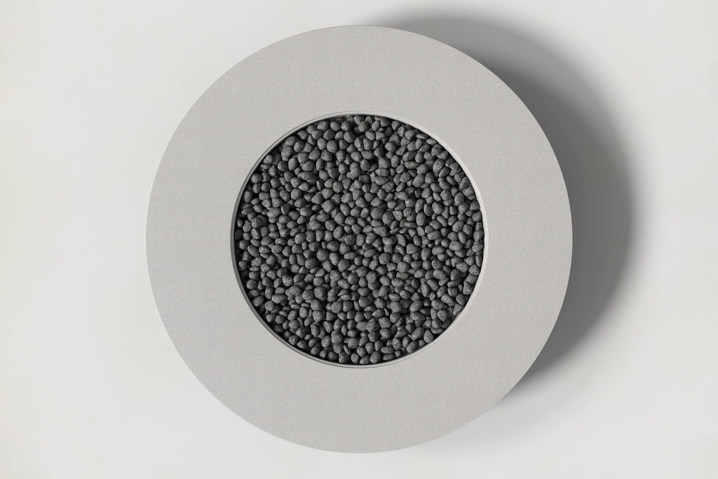 Top-down view of a circular soft grey concrete fire pit with thick walls and a circular well filled with volcanic rocks. Shown against a white background with slight shadows.