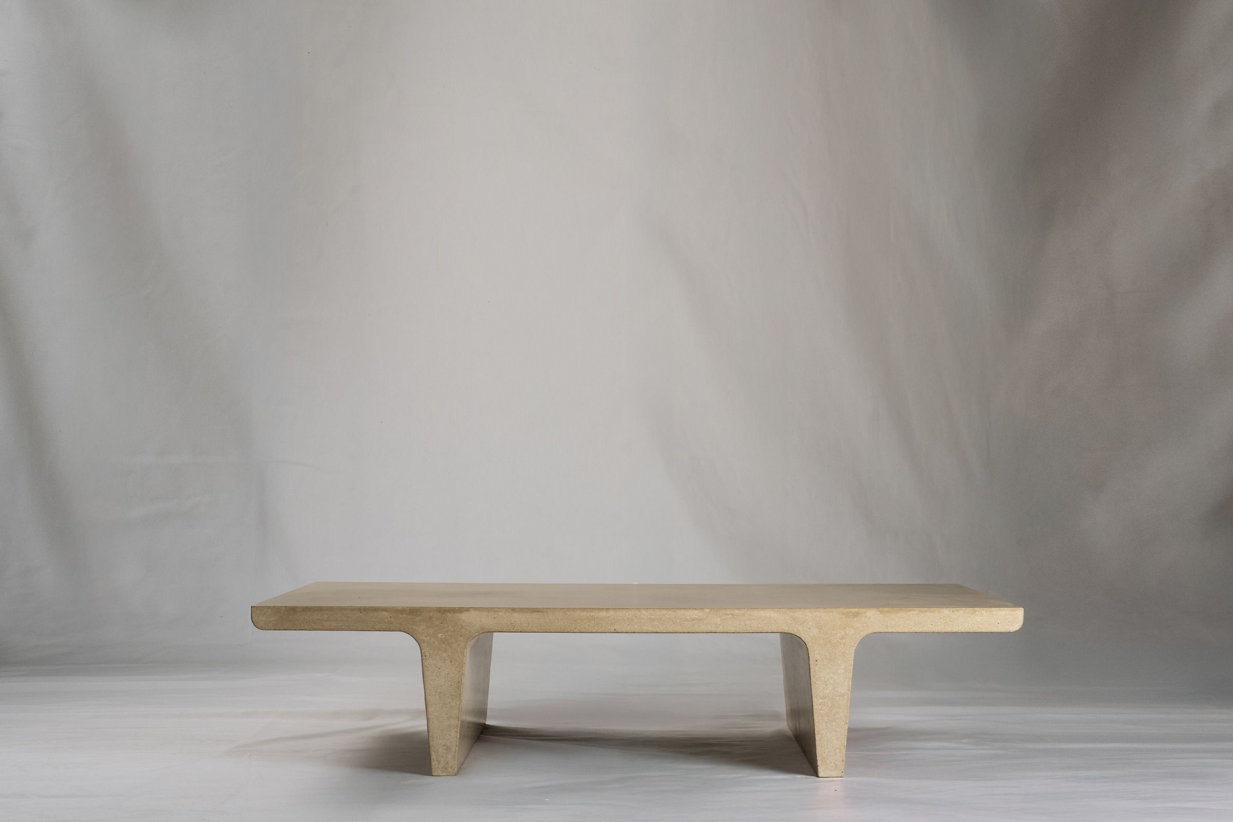 Rectangular light beige concrete coffee table with sculptural double tee legs, featuring a smooth troweled finish, set against a soft neutral backdrop.