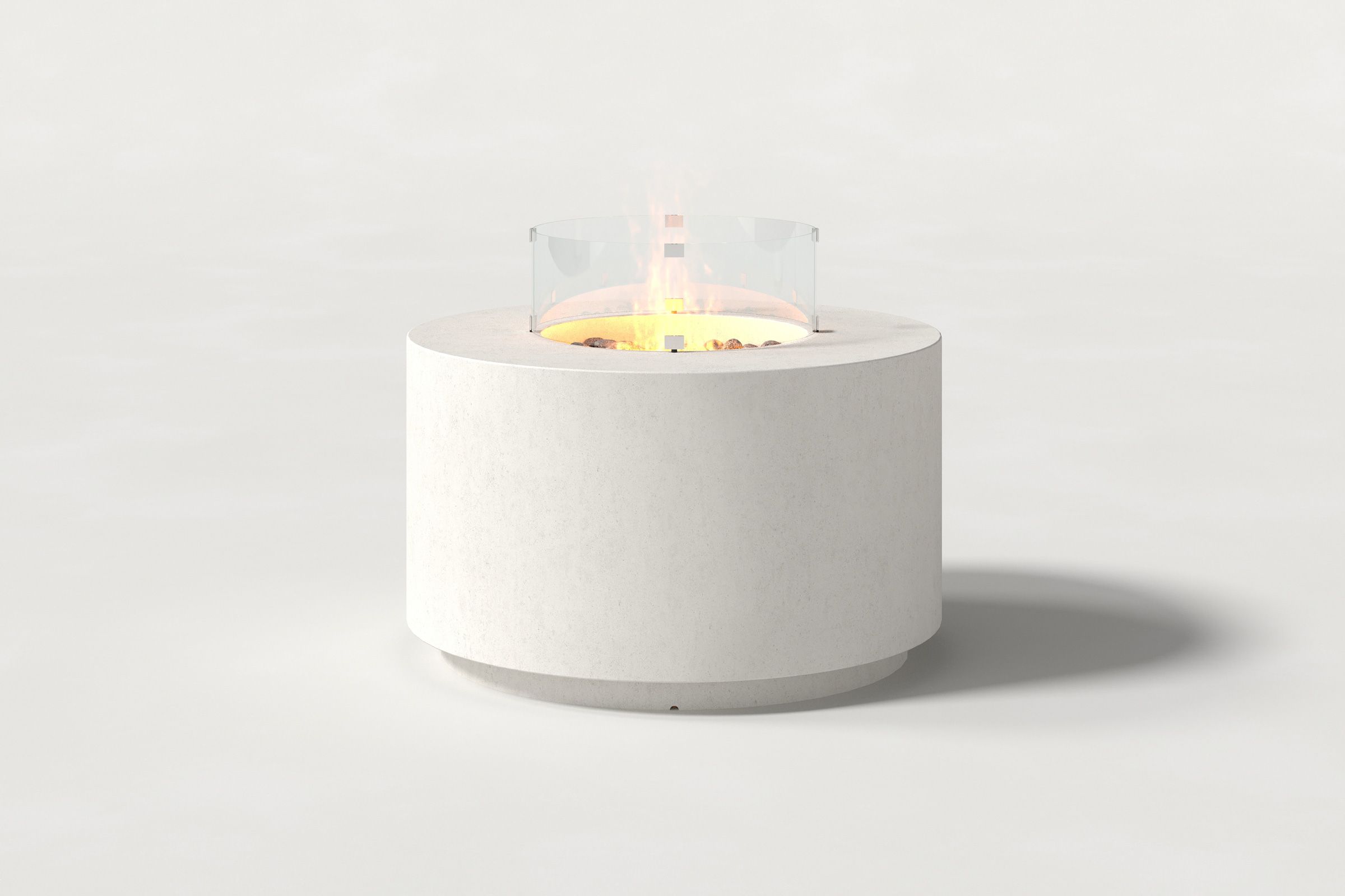 Low cylindrical white colored concrete fire pit with thick walls and a central circular well filled with dark volcanic rocks and flame, featuring an glass shield. Front view on a white background.