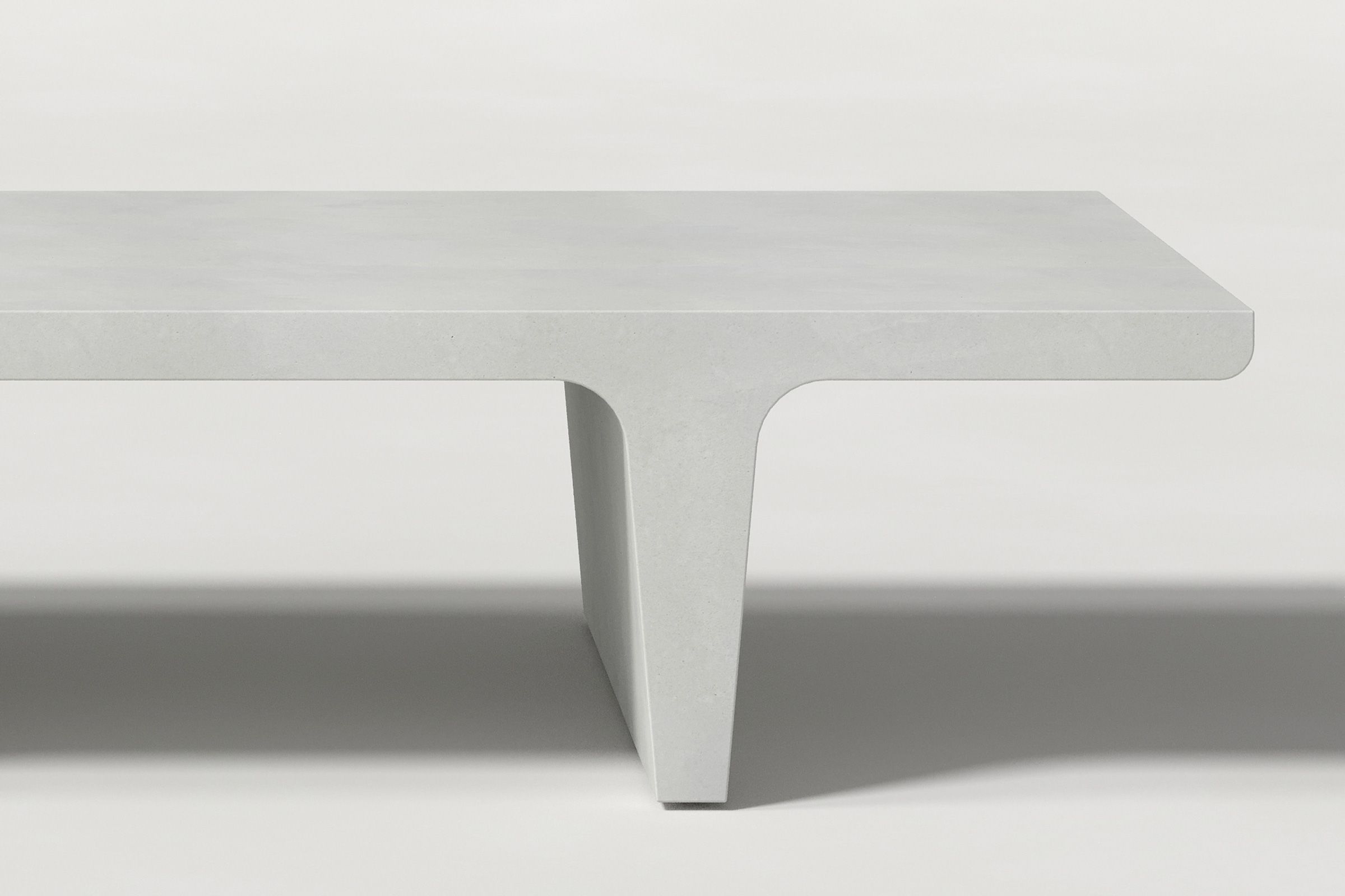 Close-up of a white concrete coffee table with sculptural double tee legs, highlighting soft edges and subtle surface texture against a clean white background.