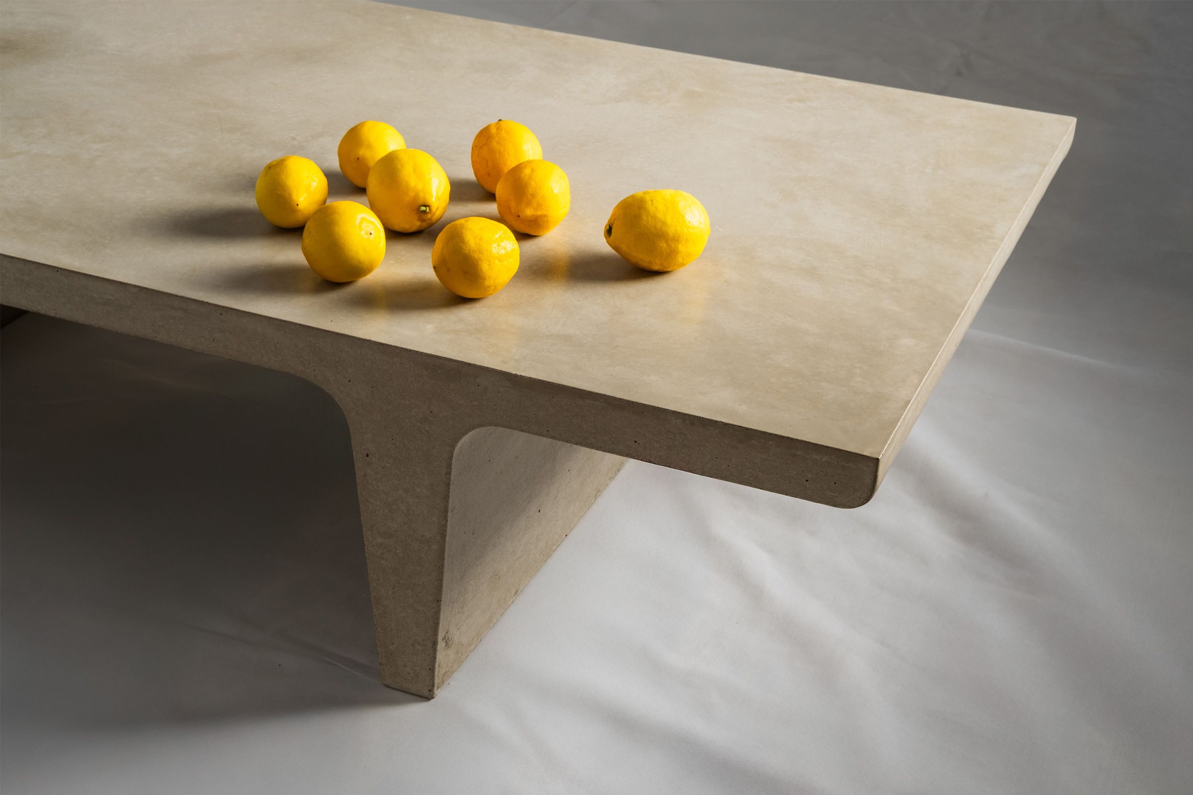 Rectangular light beige concrete coffee table with sculptural double tee legs, featuring a smooth troweled finish and styled with a small vase of flowers, set against a soft neutral backdrop.