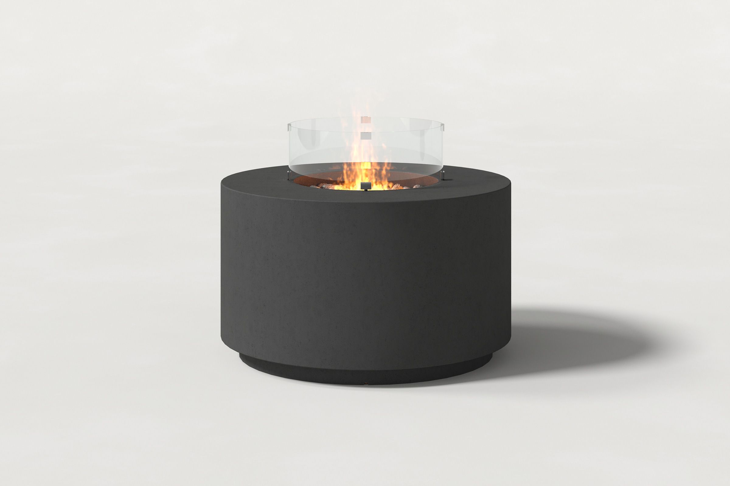 Low cylindrical charcoal colored concrete fire pit with thick walls and a central circular well filled with dark volcanic rocks and flame and glass shield. Front view on a white background.