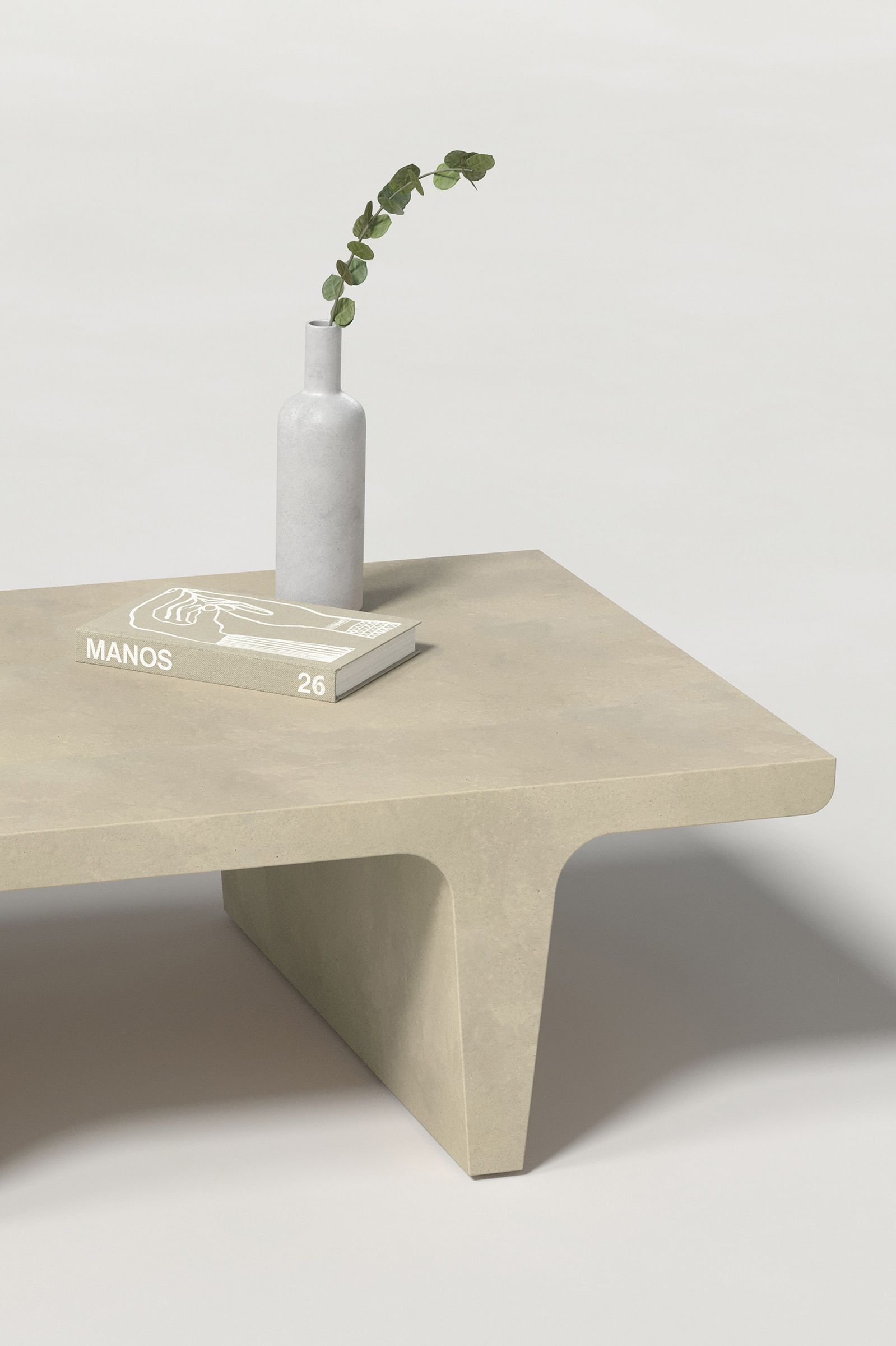 Close-up of a rectangular light beige concrete coffee table with sculptural double tee legs, styled with a neutral-toned book and a slender vase holding a eucalyptus, set against a clean white background.