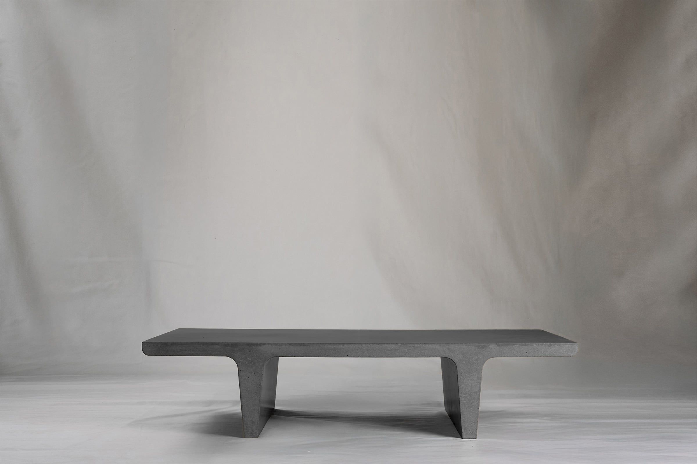 Rectangular dark grey concrete coffee table with sculptural double tee legs, featuring a smooth troweled finish, set against a soft neutral backdrop.