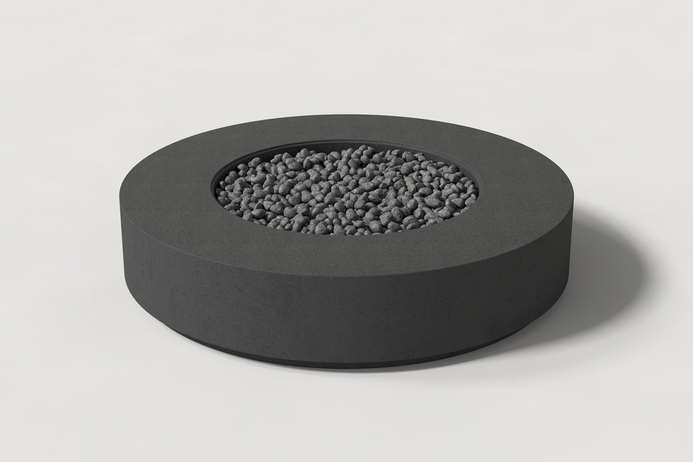 Low cylindrical charcoal concrete fire pit with thick walls and a central circular well. Mid-range angle shows the well filled with volcanic rocks against a white background.