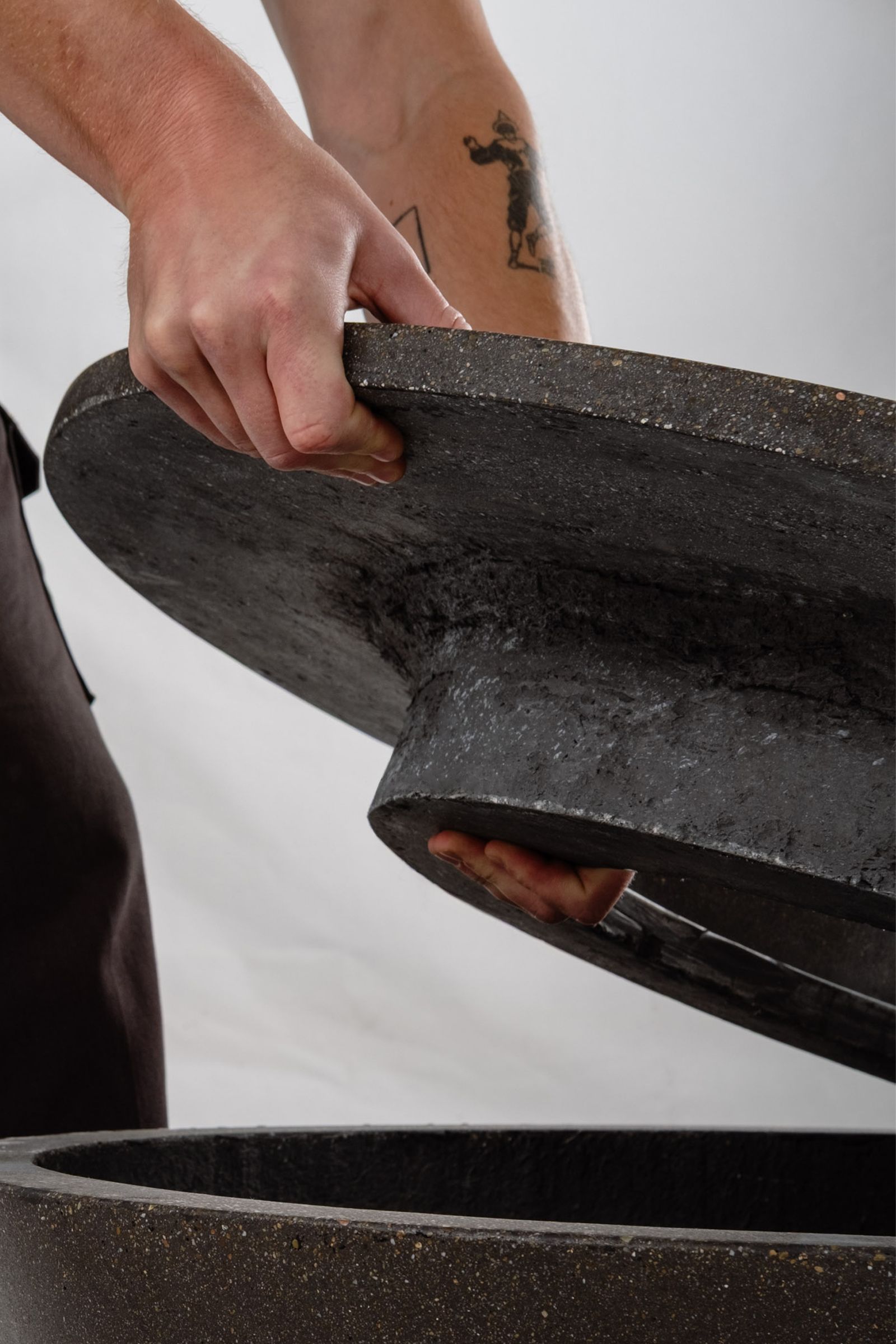 Close-up lifting the rim of the Rosa fire pit, a round dark grey concrete fire pit with etched sides.