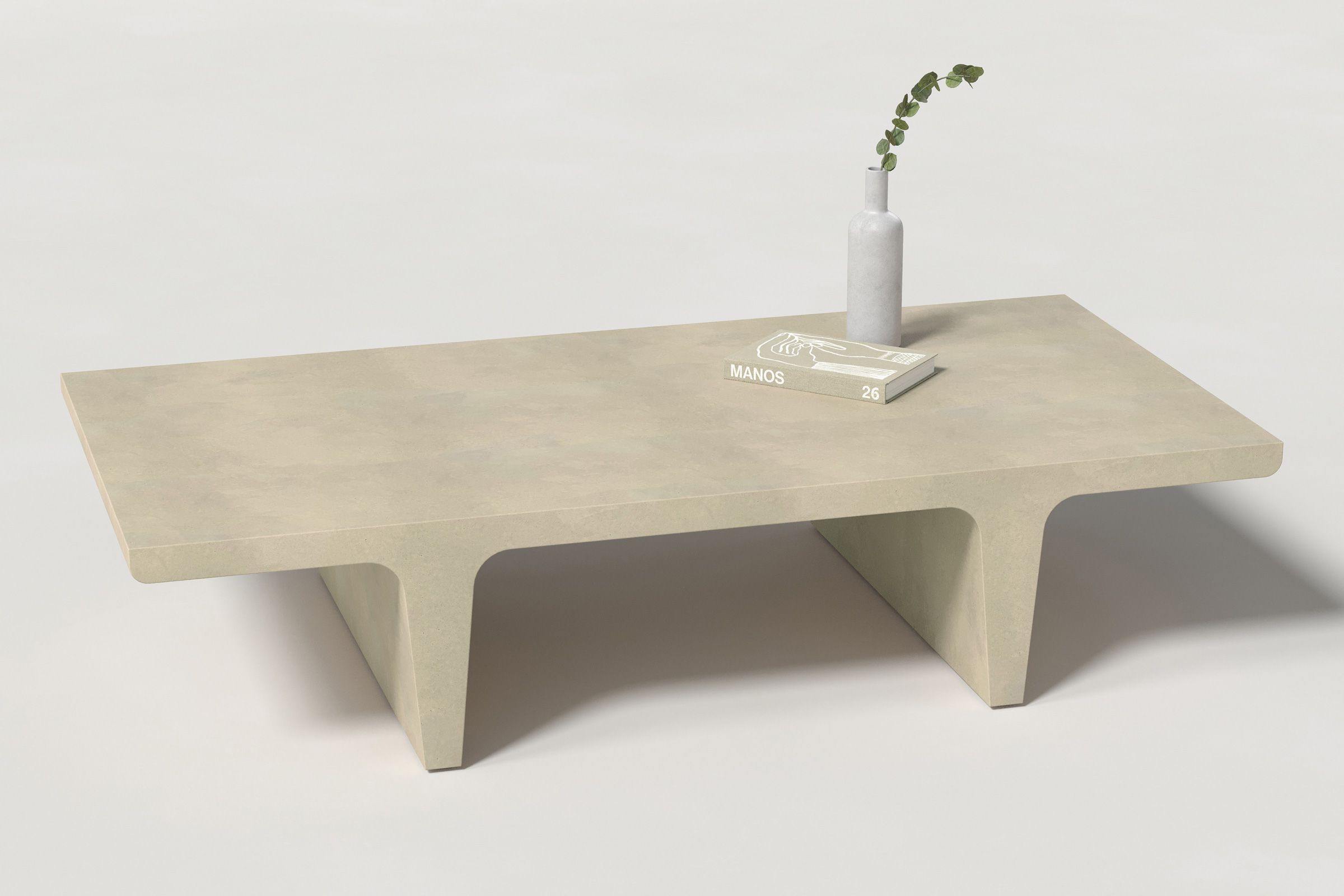 A rectangular light beige concrete coffee table with sculptural double tee legs, styled with a neutral-toned book and a slender vase holding a eucalyptus, set against a clean white background.