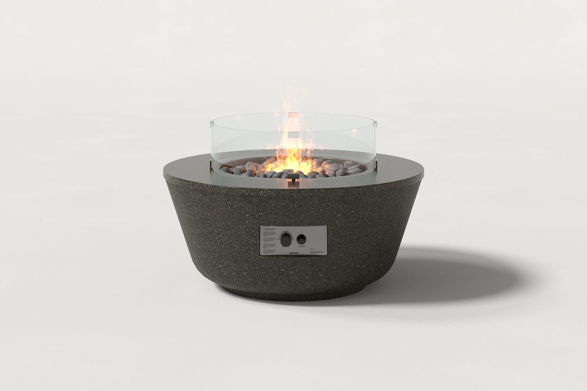 Round dark grey concrete fire pit with a honed top and etched sides, featuring a glass shield and lava rocks with an active flame, set against a clean white background.