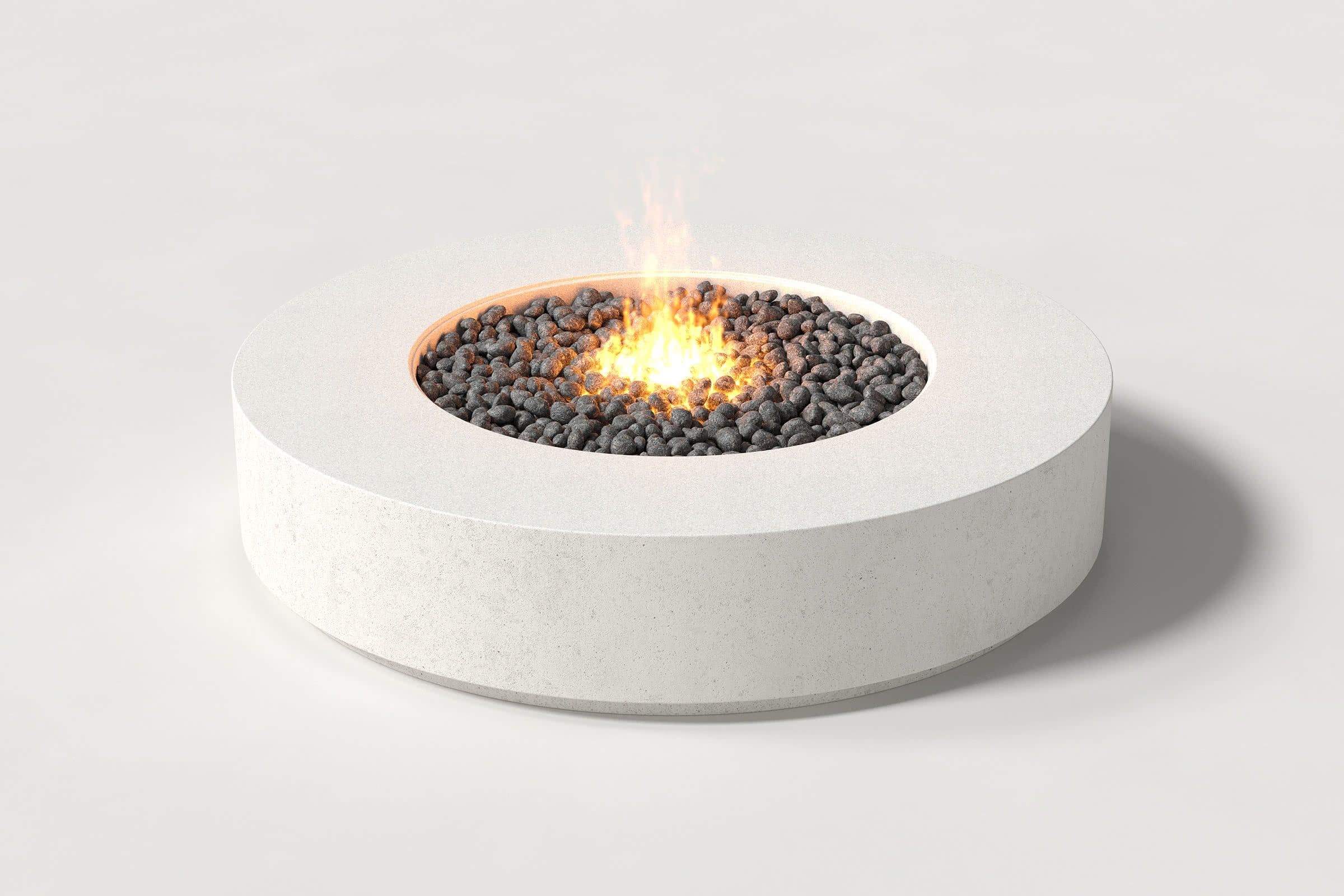 Low cylindrical white concrete fire pit with thick walls and a central circular well. Mid-range angle shows the well filled with flaming volcanic rocks against a white background.