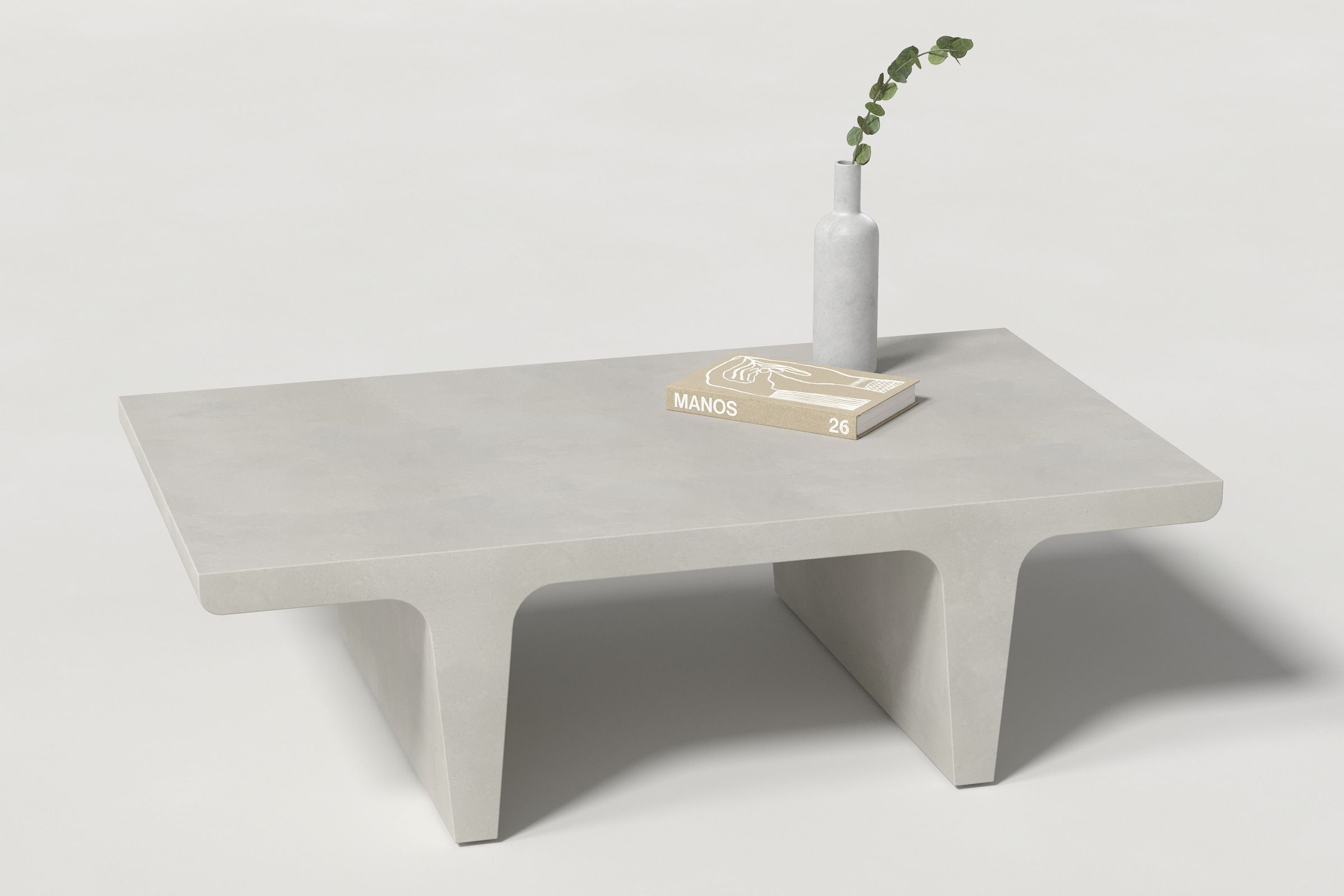 A rectangular light grey concrete coffee table with sculptural double tee legs, styled with a neutral-toned book and a slender vase holding a eucalyptus, set against a clean white background.