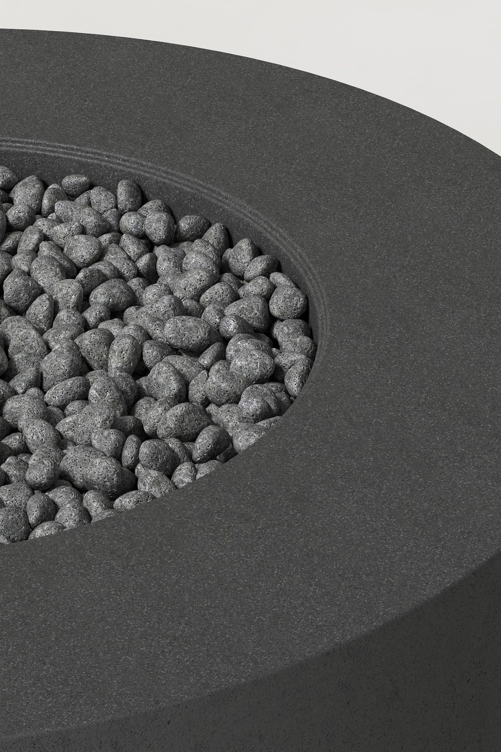 Close-up photograph of a cylindrical charcoal concrete fire pit with thick walls and a well filled with volcanic rocks. Showcases a smooth texture and precise edge design.