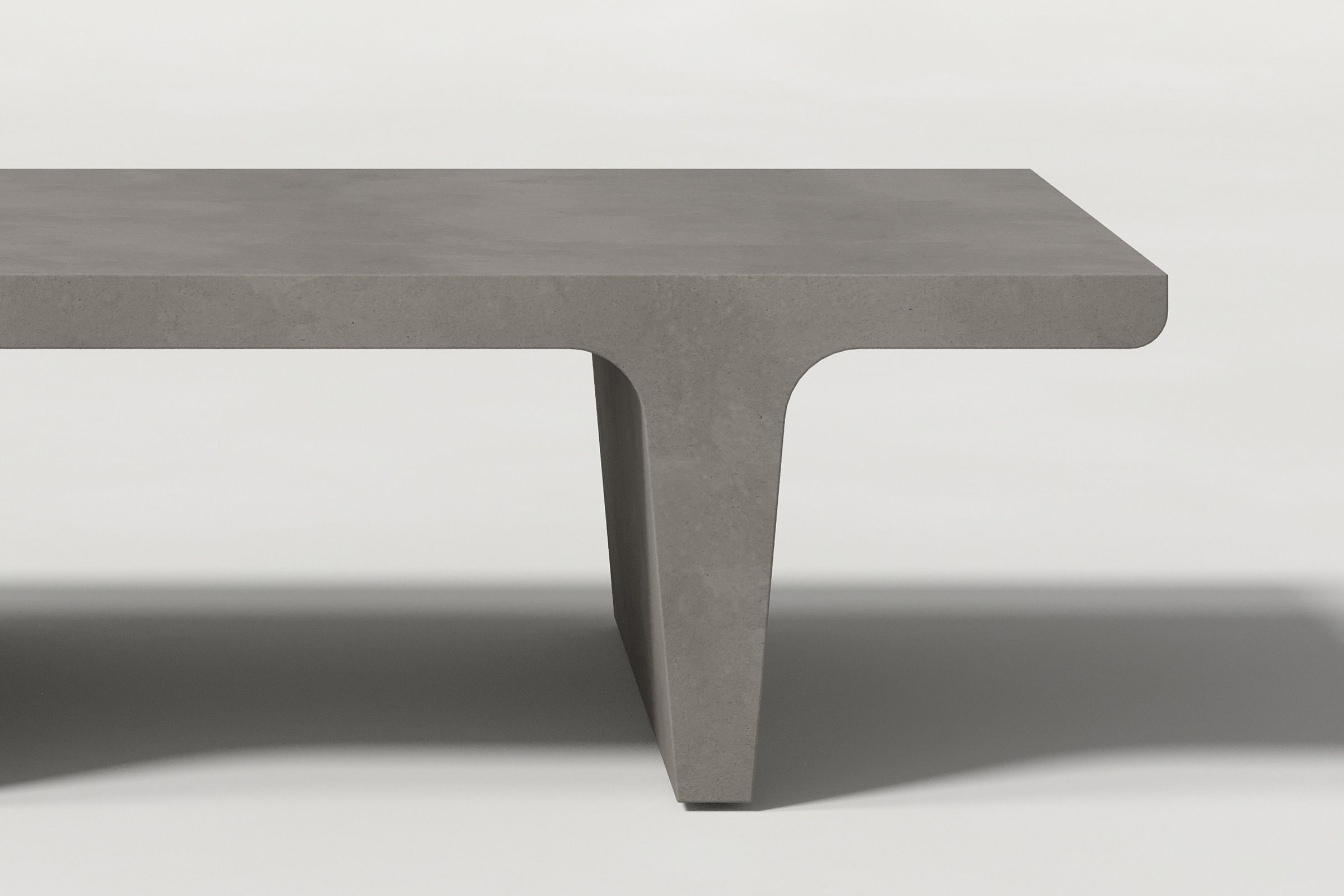 Close-up of a dark grey concrete coffee table with sculptural double tee legs, highlighting soft edges and subtle surface texture against a clean white background.