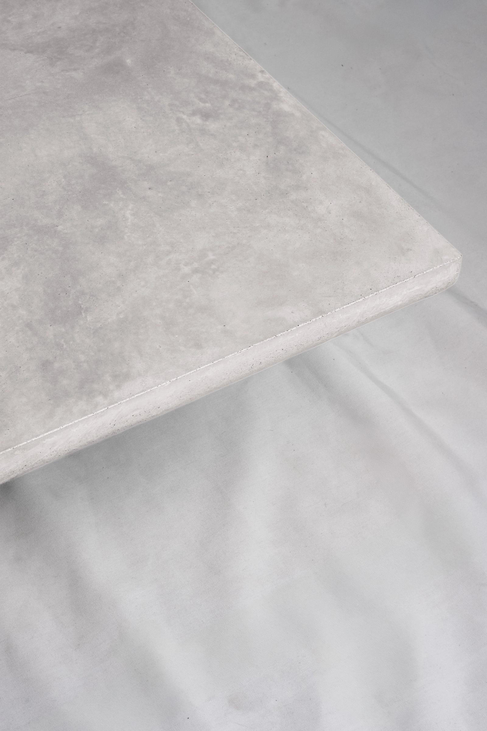 A close up of a light grey concrete coffee table edge, featuring a smooth troweled finish, set against a soft neutral backdrop.