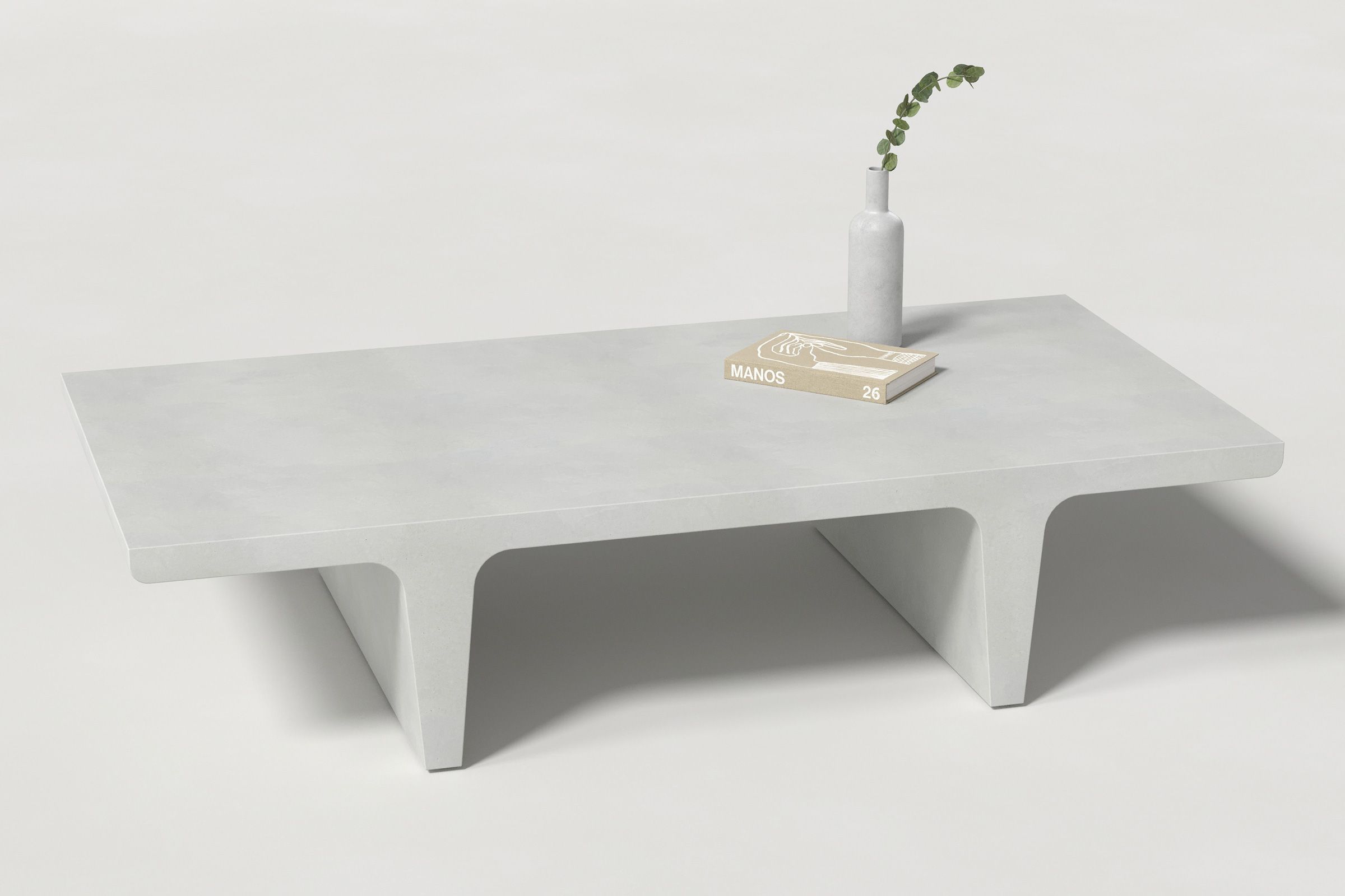 A rectangular white concrete coffee table with sculptural double tee legs, styled with a neutral-toned book and a slender vase holding a eucalyptus, set against a clean white background.