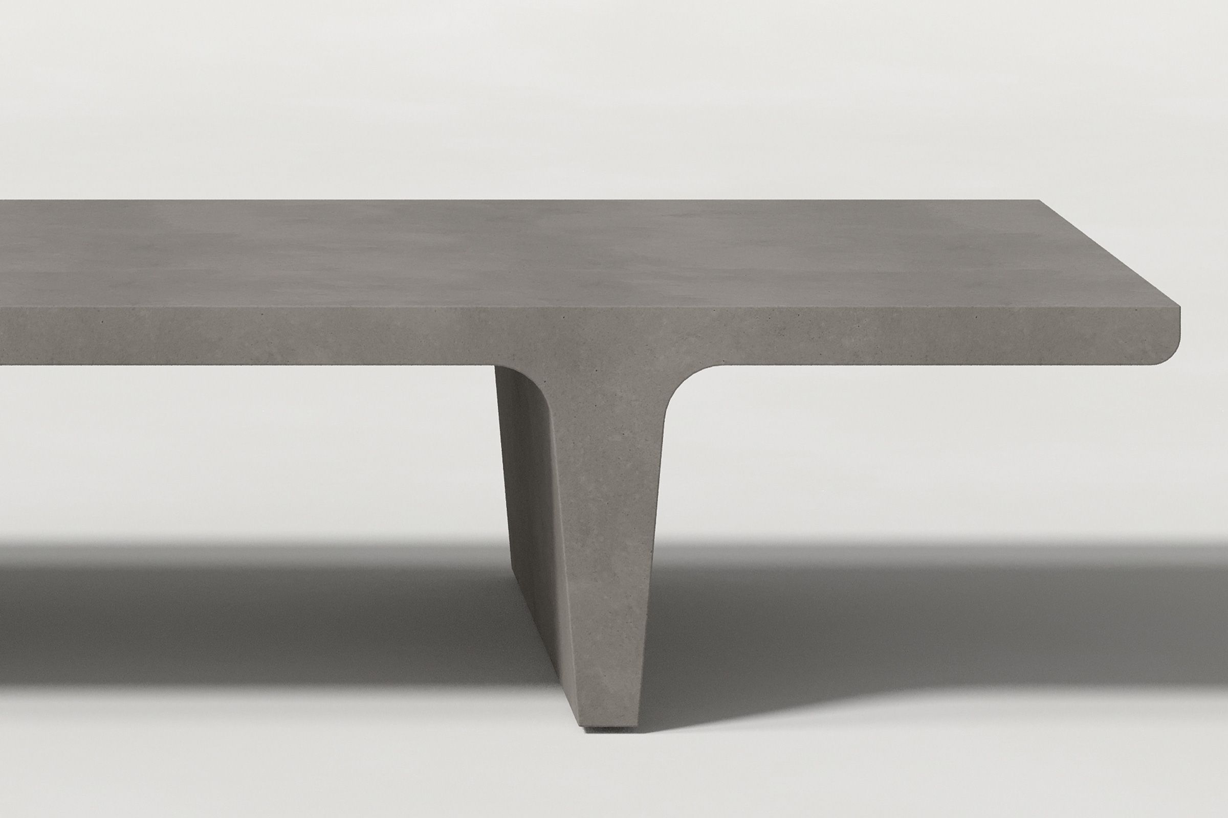 Close-up of a dark grey concrete coffee table with sculptural double tee legs, highlighting soft edges and subtle surface texture against a clean white background.