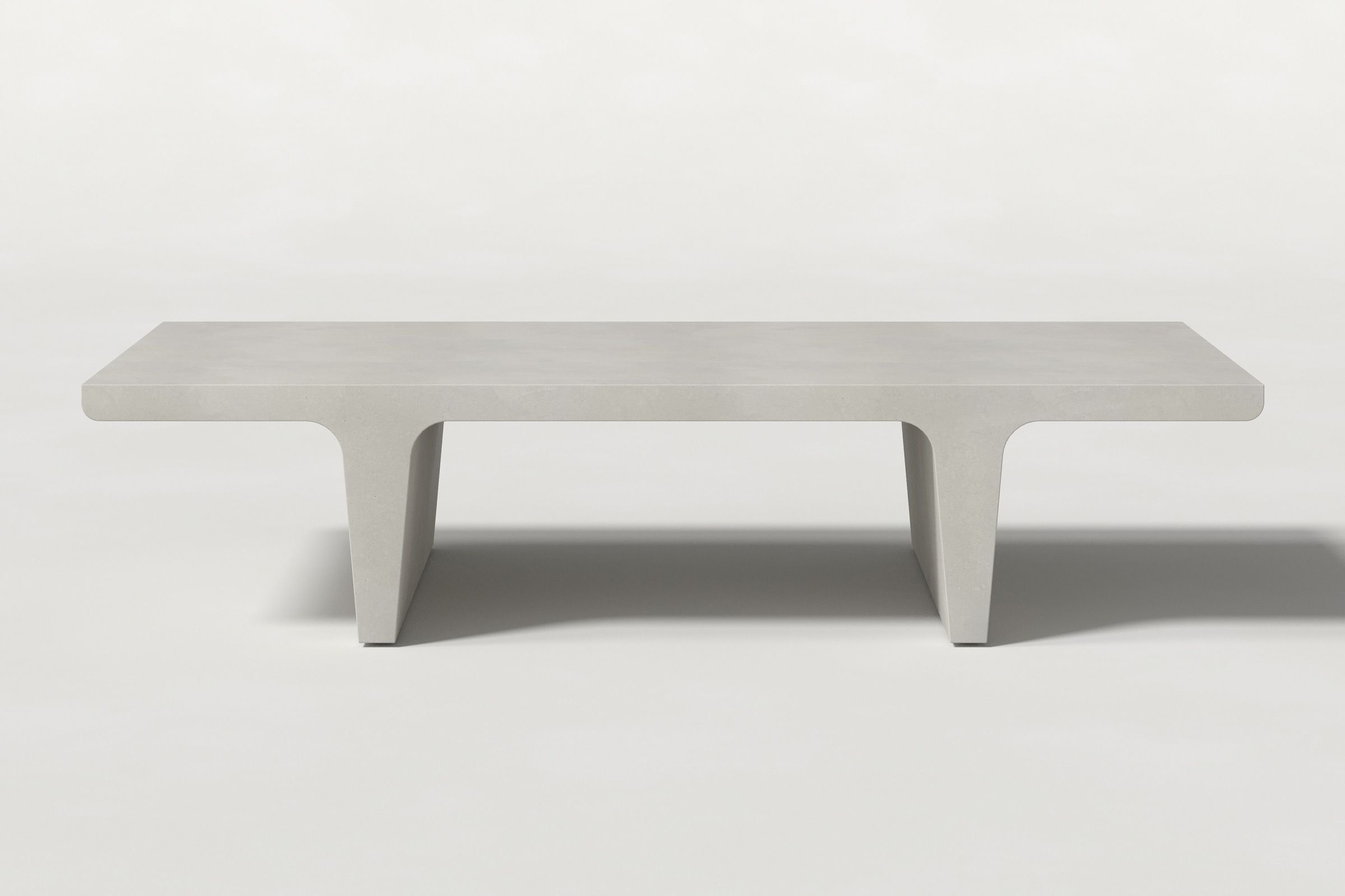 Close-up of a light grey concrete coffee table with sculptural double tee legs, highlighting soft edges and subtle surface texture against a clean white background.