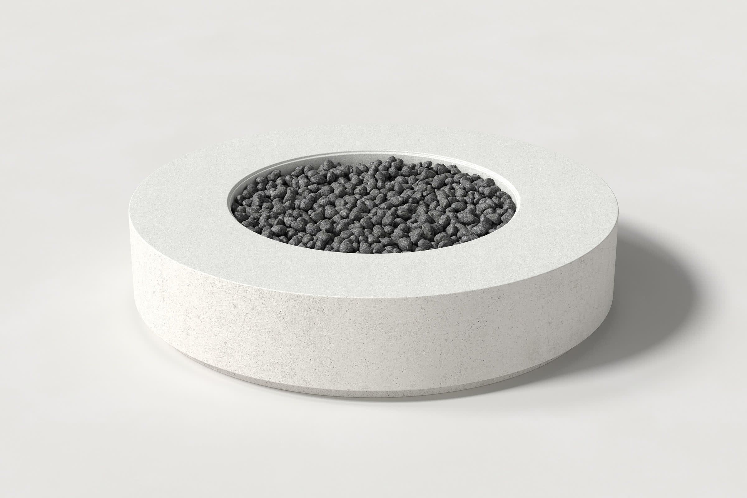 Low cylindrical white concrete fire pit with thick walls and a central circular well. Mid-range angle shows the well filled with volcanic rocks against a white background.