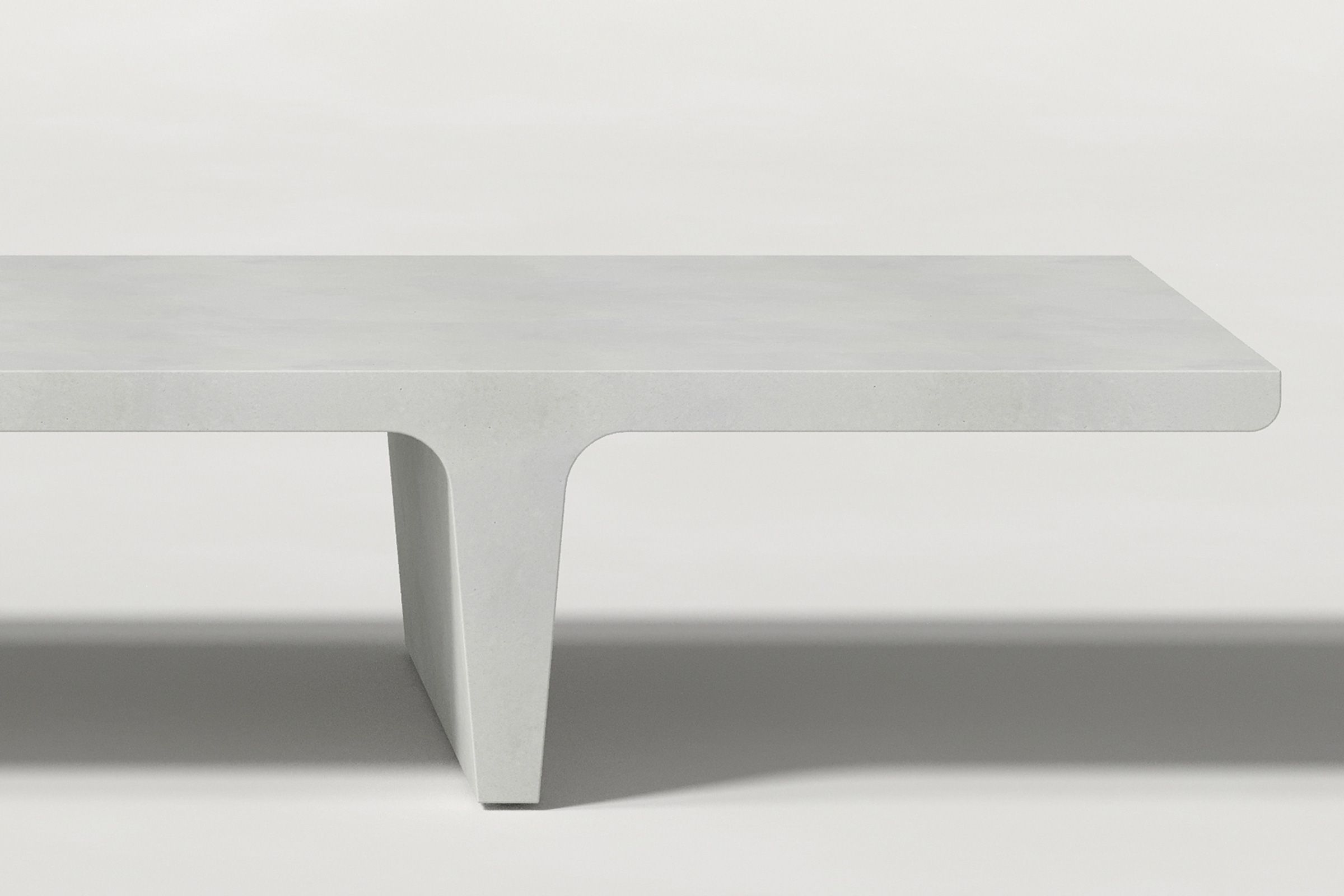 Close-up of a white concrete coffee table with sculptural double tee legs, highlighting soft edges and subtle surface texture against a clean white background.