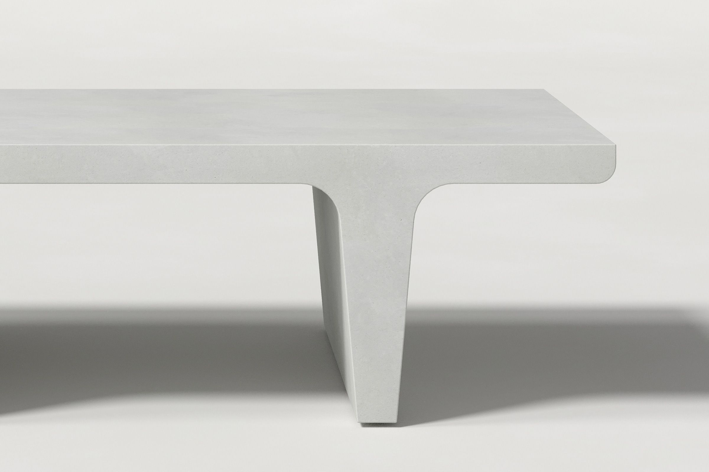 Close-up of a white concrete coffee table with sculptural double tee legs, highlighting soft edges and subtle surface texture against a clean white background.