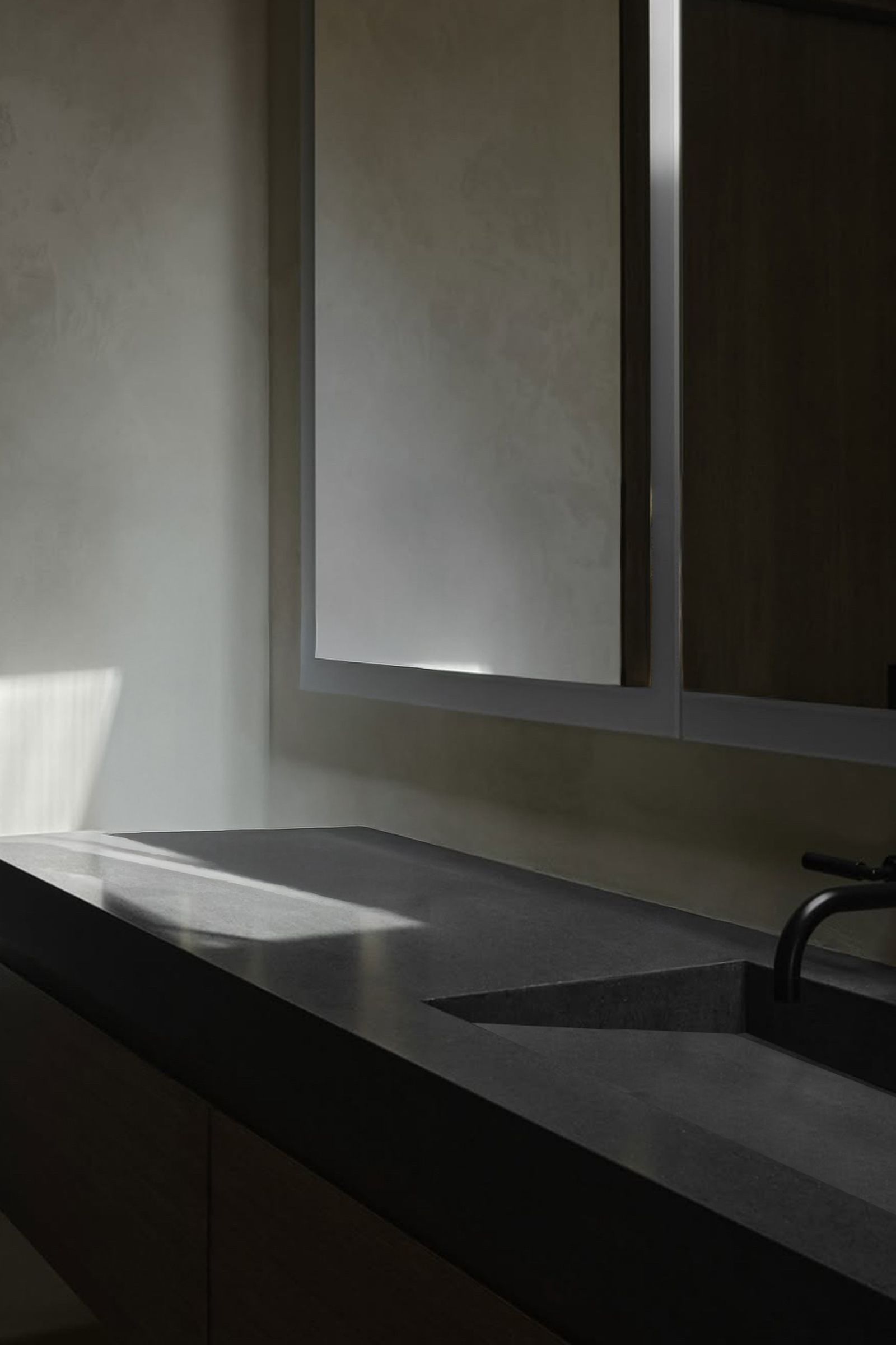 Dark concrete vanity with integrated sink, black faucet, and mirror in soft sunlight.